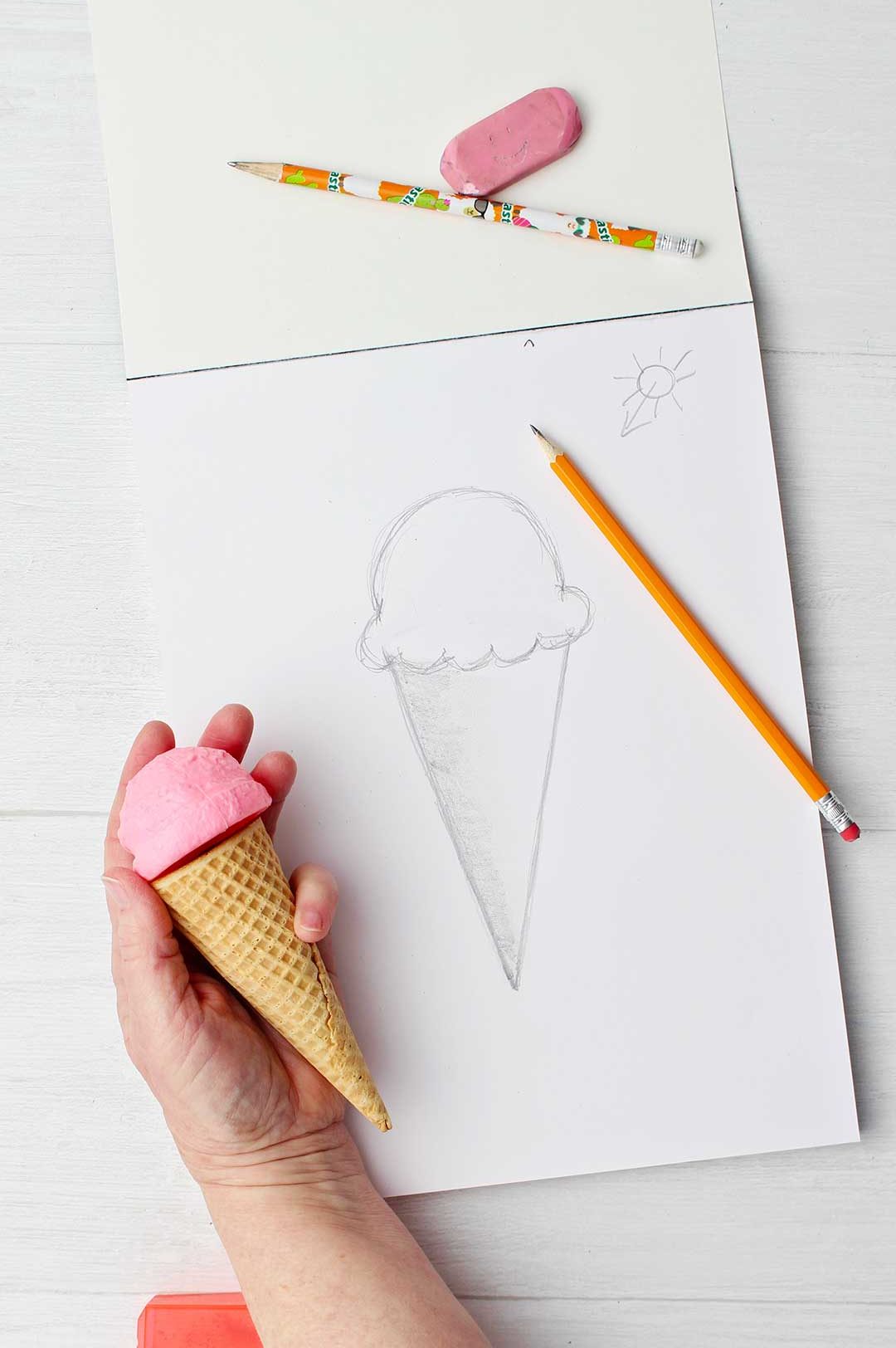 Hand holding a 3D ice cream cone comparing it to a quick sketch of an ice cream cone done in pencil.
