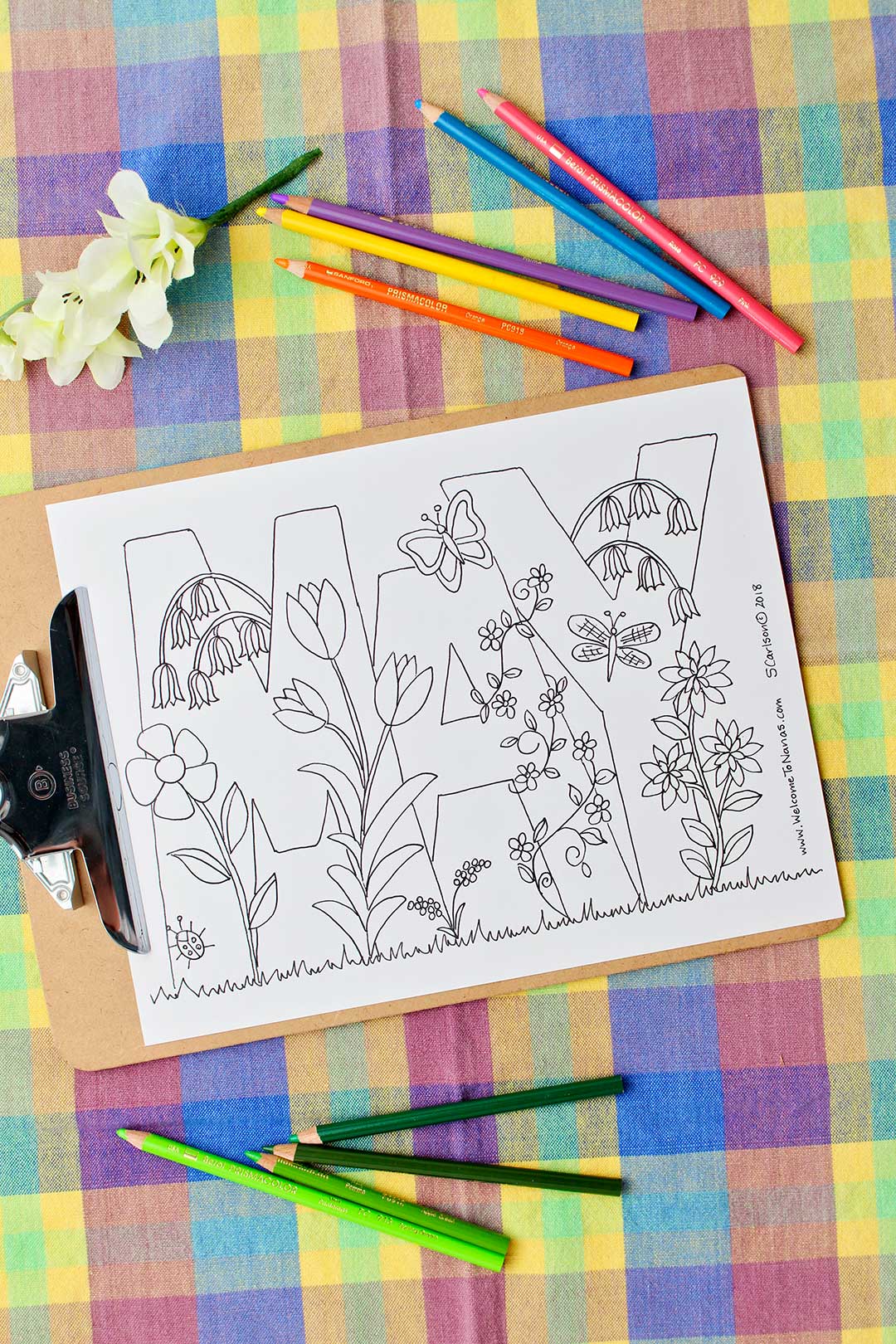 Uncolored May Coloring page clipped to a clip board resting on a colorful plaid background.