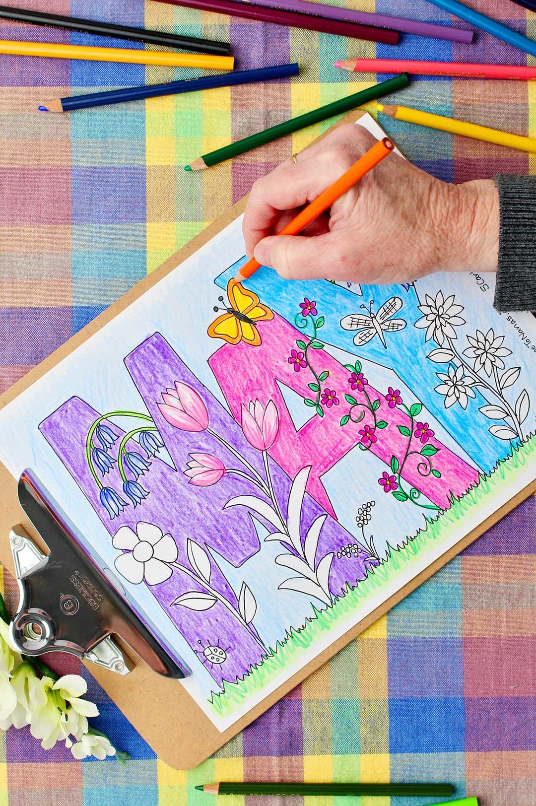 Hand coloring butterfly wings orange in May Coloring Page with colored pencils resting on a colorful plaid background.