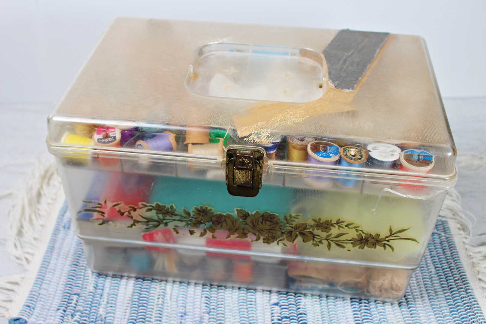 Vintage plastic sewing box filled with spools of thread and various sewing tools.