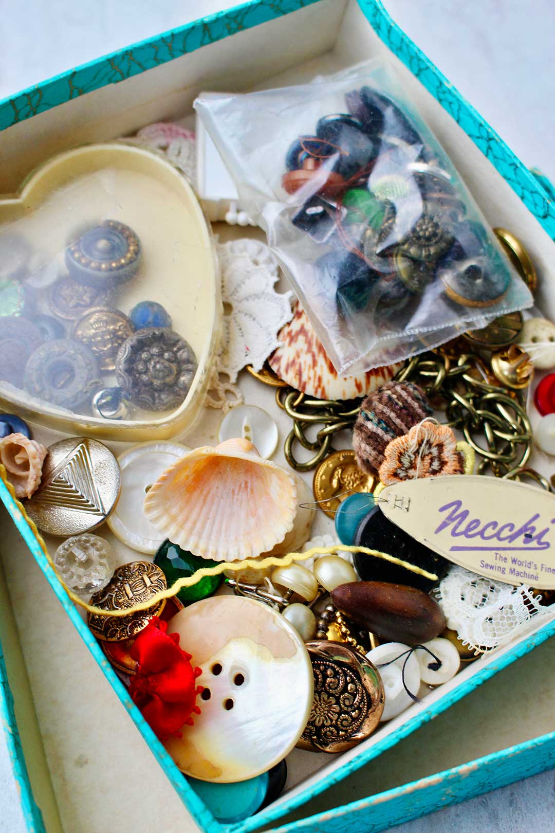 Inside of an old box of items like vintage buttons, old chains, and shells.