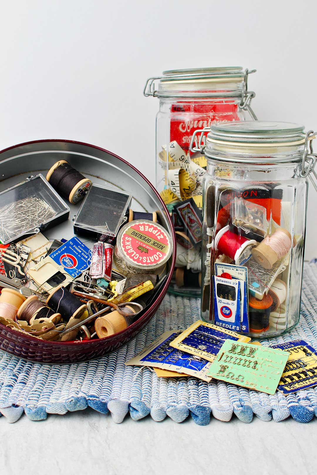 Metal cookie tin filled with odds and ends and two glass jars filled with sewing box treasures.