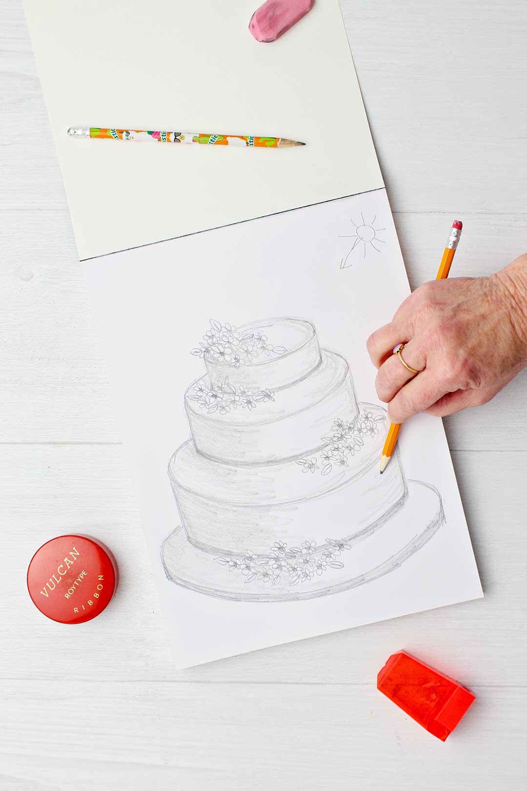Hand sketching some shadowing on right side of third tier of wedding cake.
