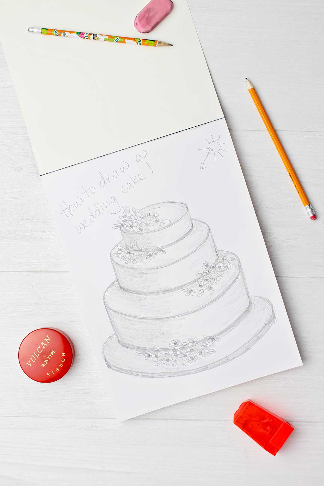 Final complete drawing of a wedding cake with pencil sharpener and pink eraser near by.