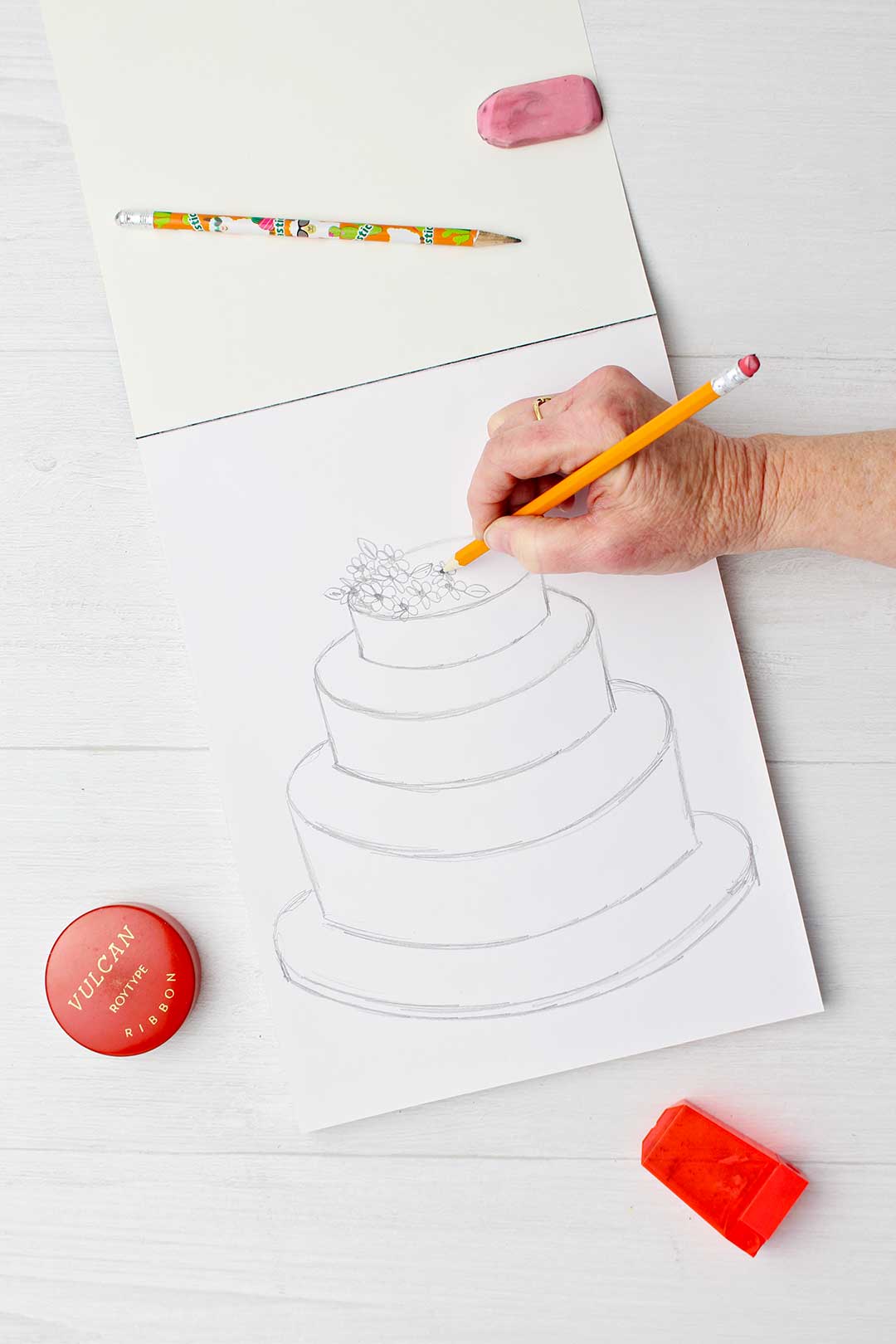 Hand sketching flowers on top of wedding cake.