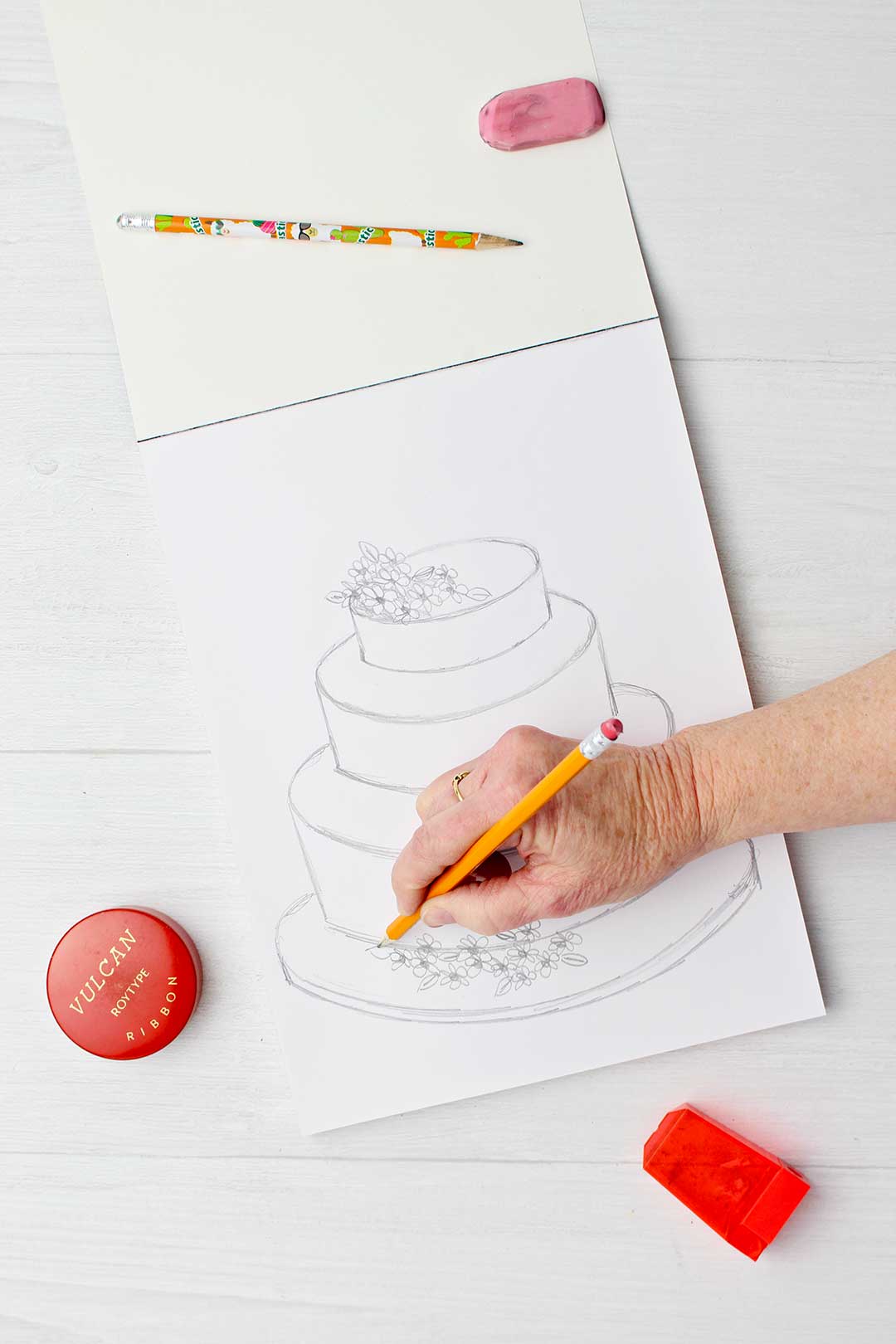 Hand sketching flowers on bottom of wedding cake.