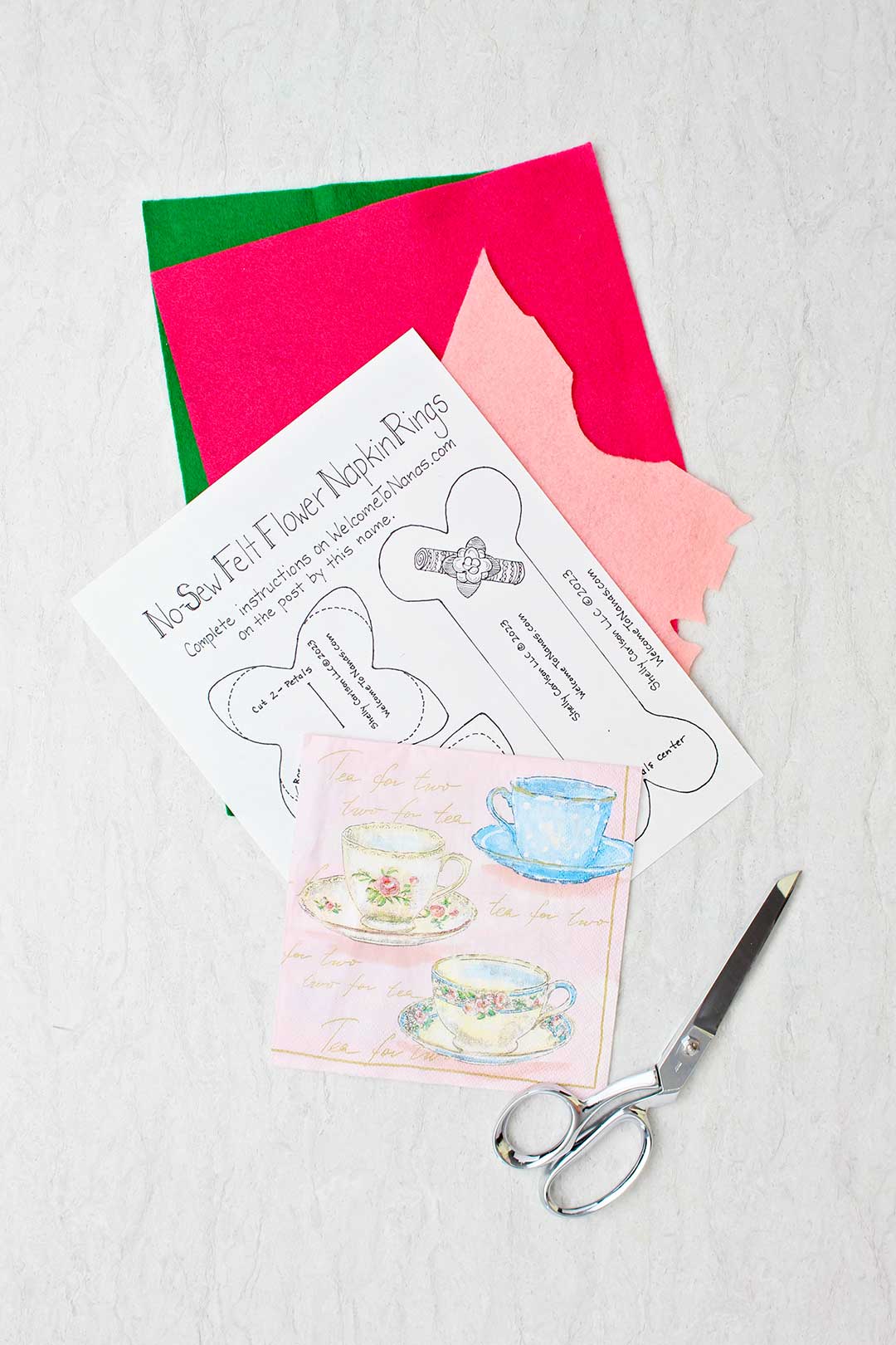 Green, dark pink and light pink felt, paper pattern, teacup napkin and scissors.