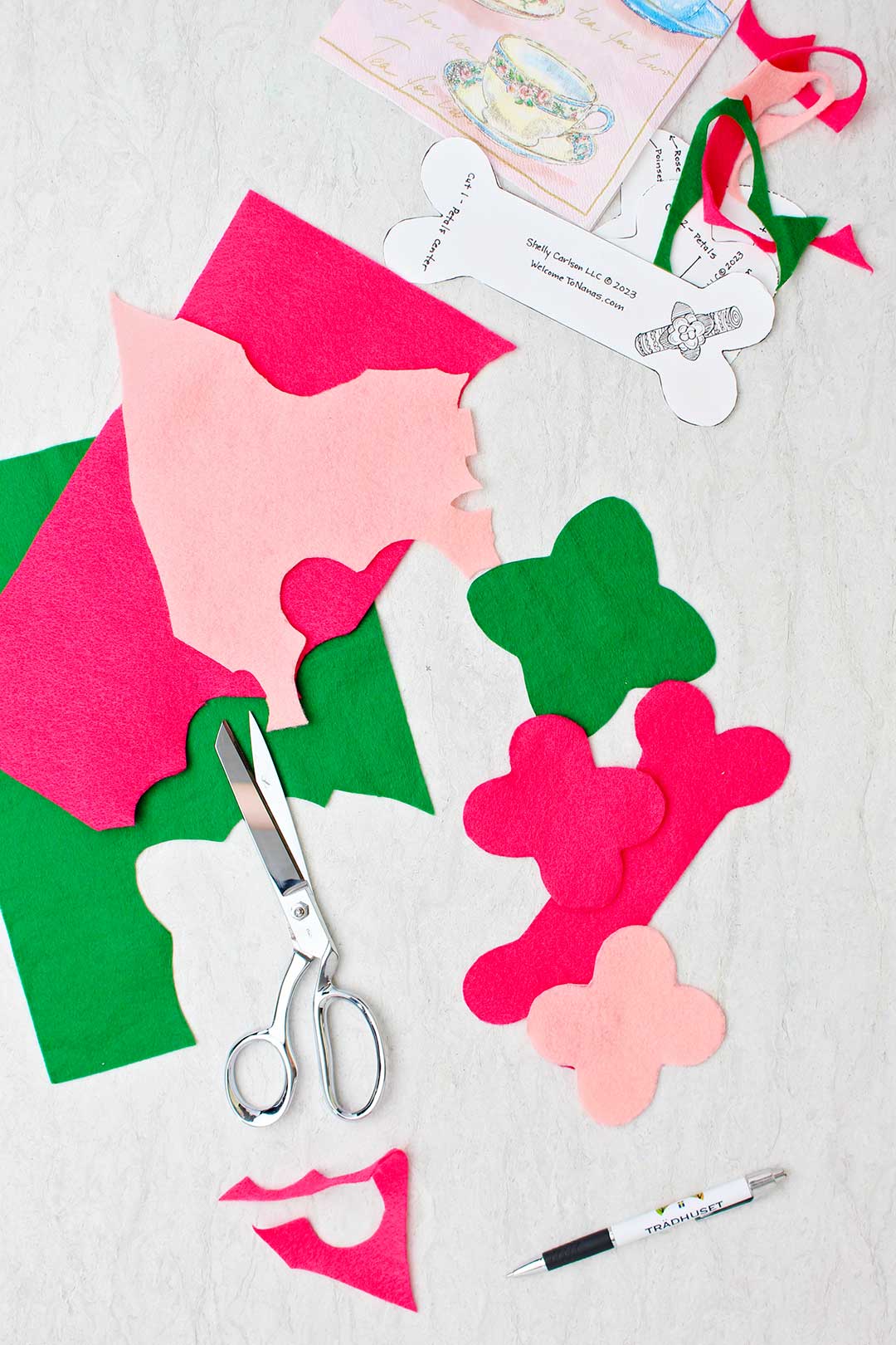 Cut out pieces of felt in green and pink with pattern, pen and scissors resting near by.