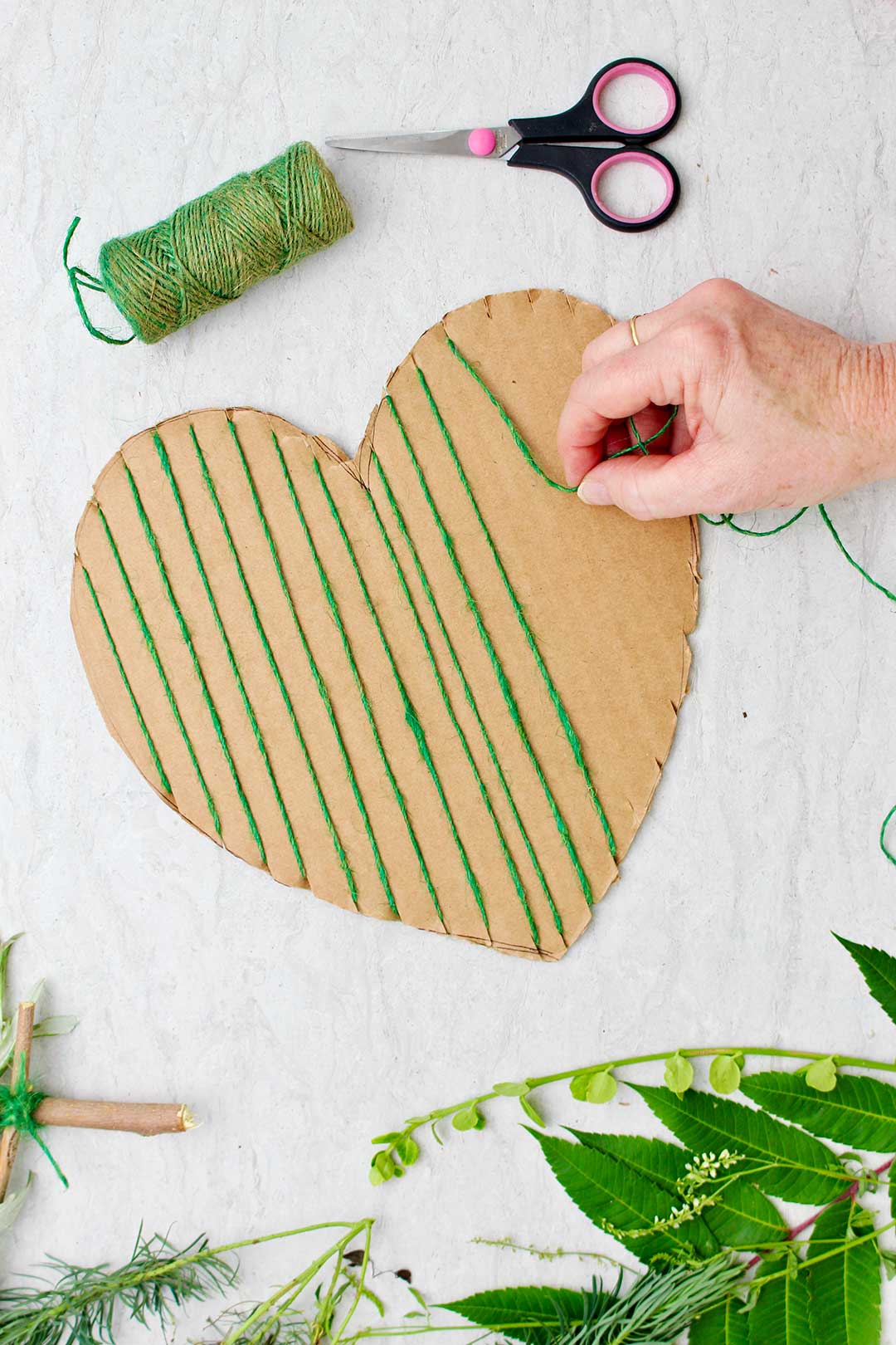 Hand securing green string on heart shaped cardboard.