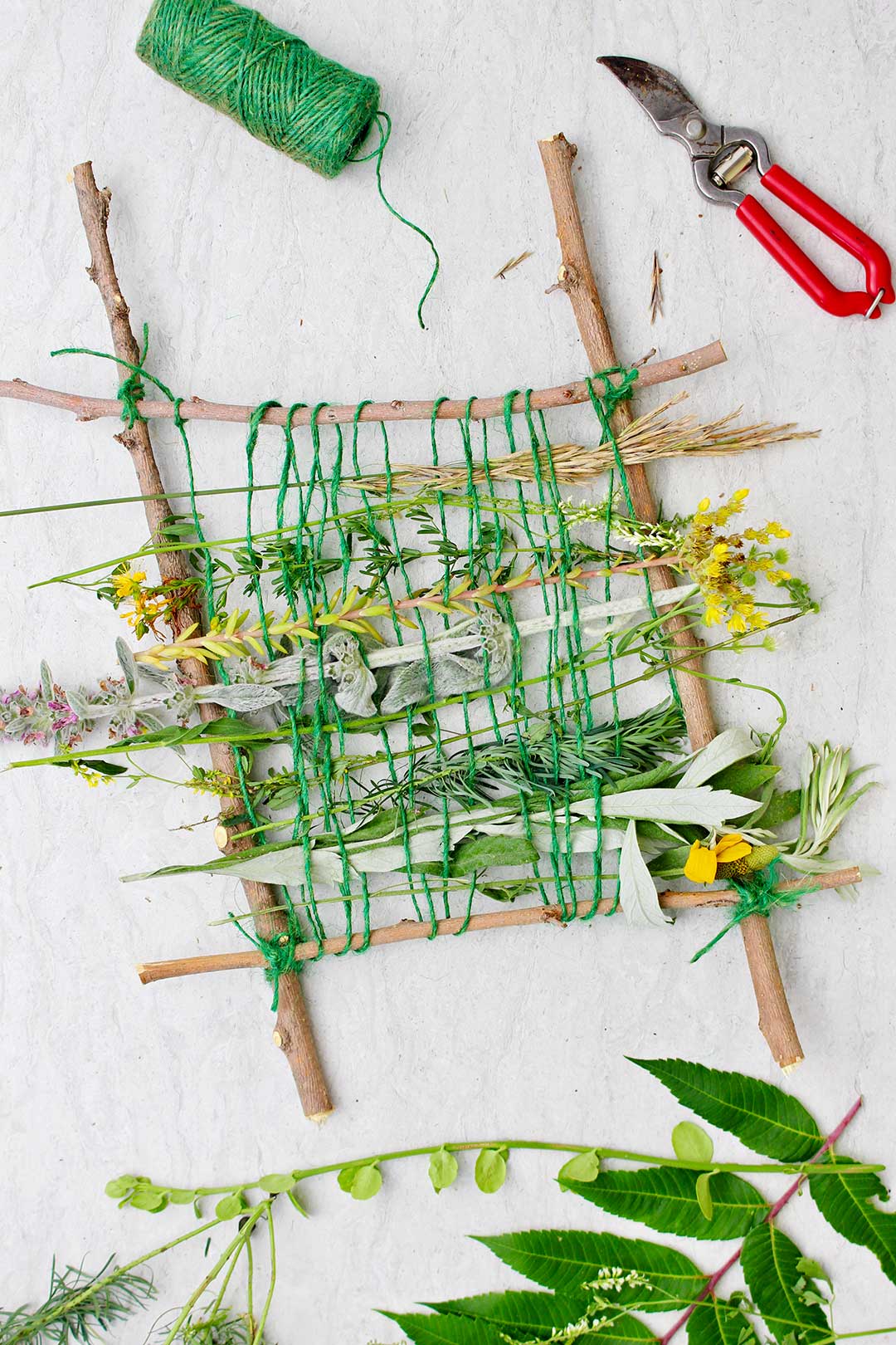 Completed nature weave using flowers and springs of various greenery on a twig loom with green string.