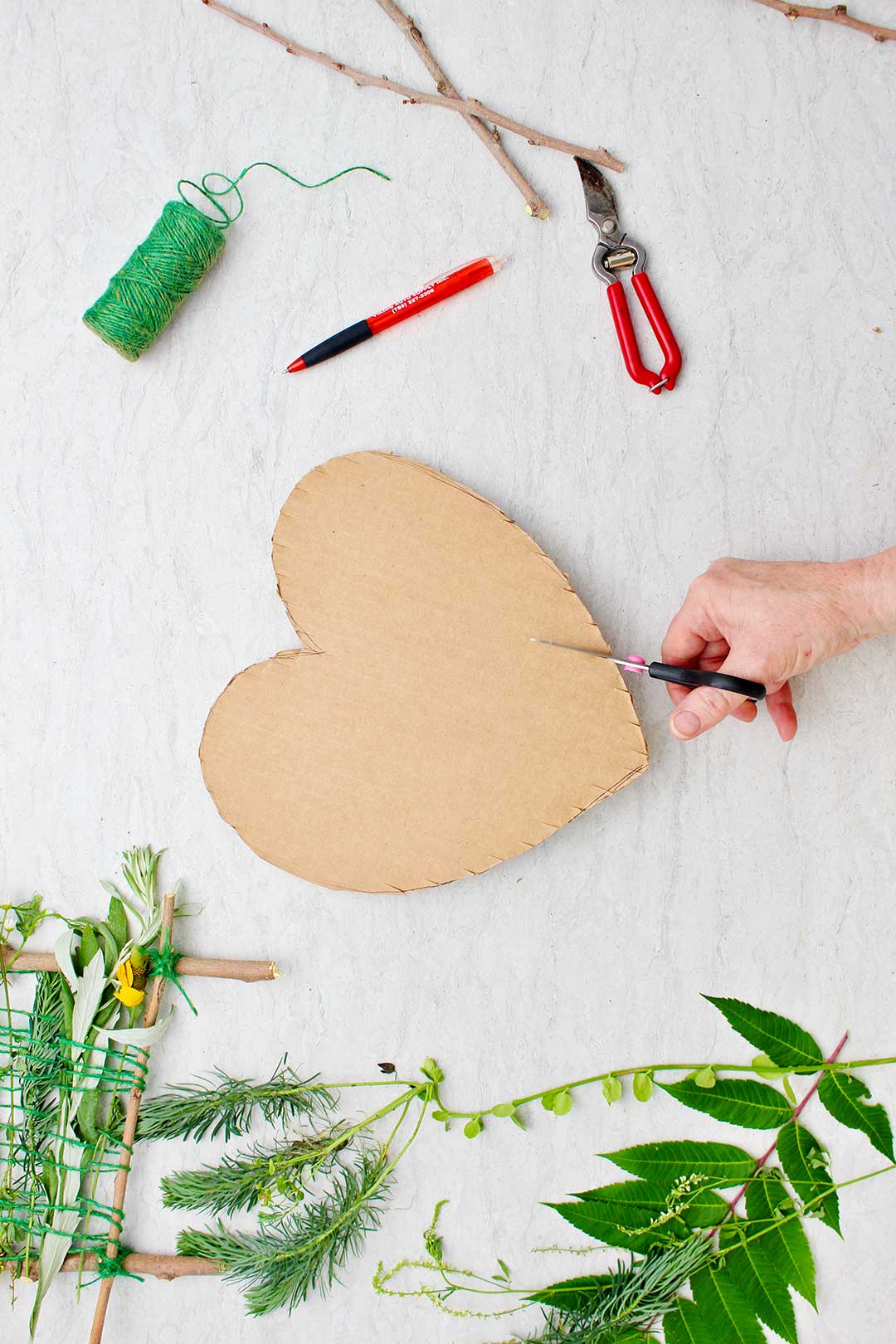 Hand cutting notches in heart shaped cardboard with supplies near by.