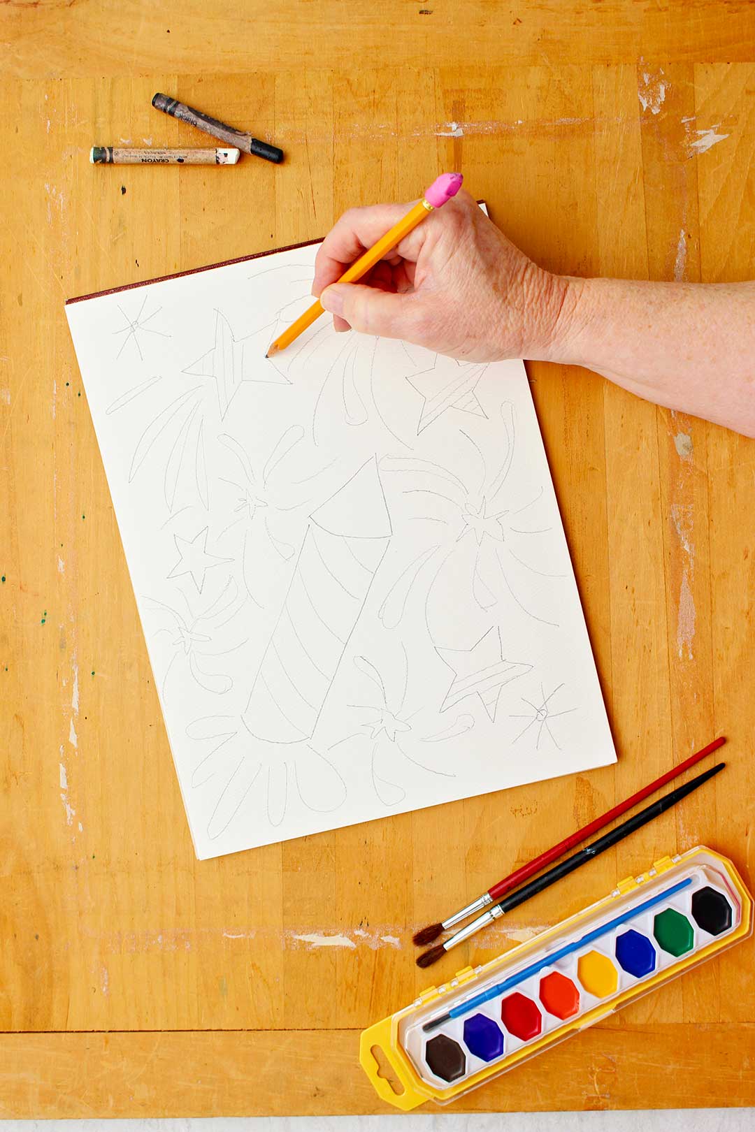 Hand sketching outline of drawing of stars and rockets for the watercolor resist.