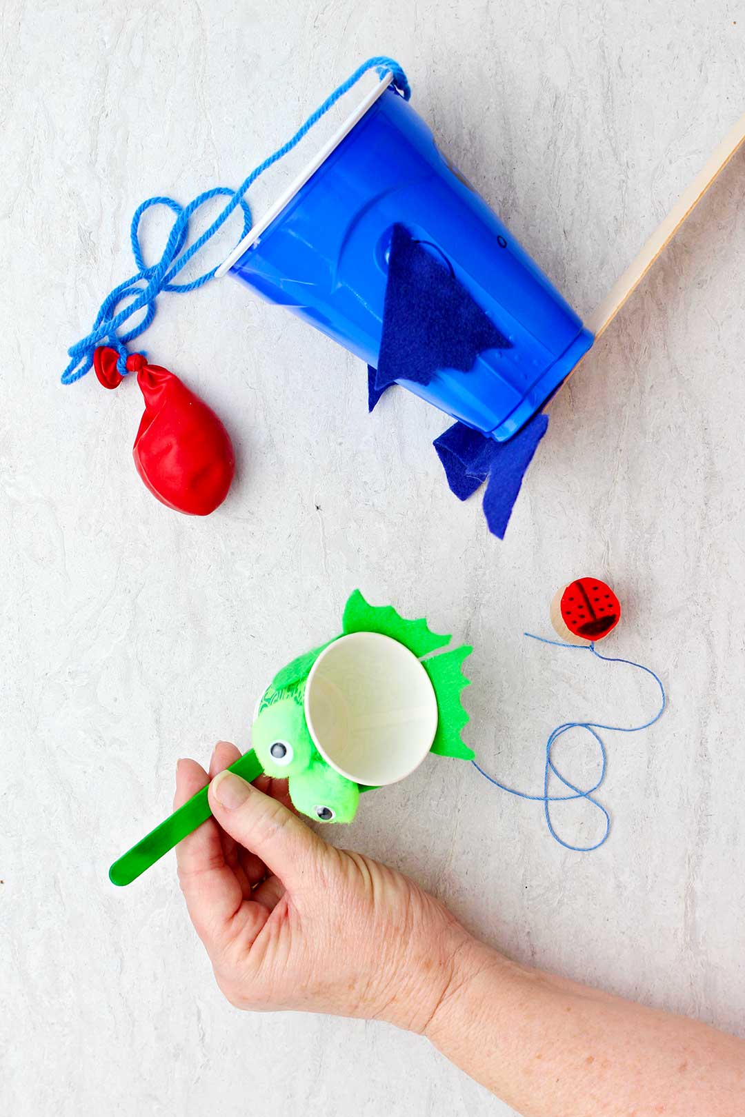 Hand holding completed green frog Ball in Cup Game with blue shark one near by.