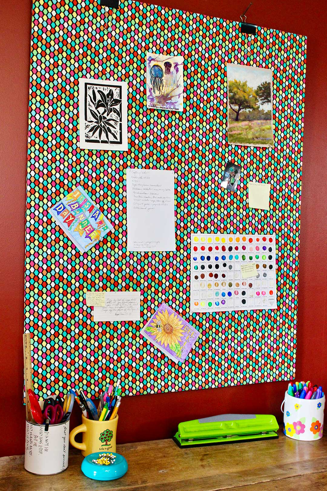 Polka dotted fabric bulletin board secured to a red wall with various cards and papers pinned to it.