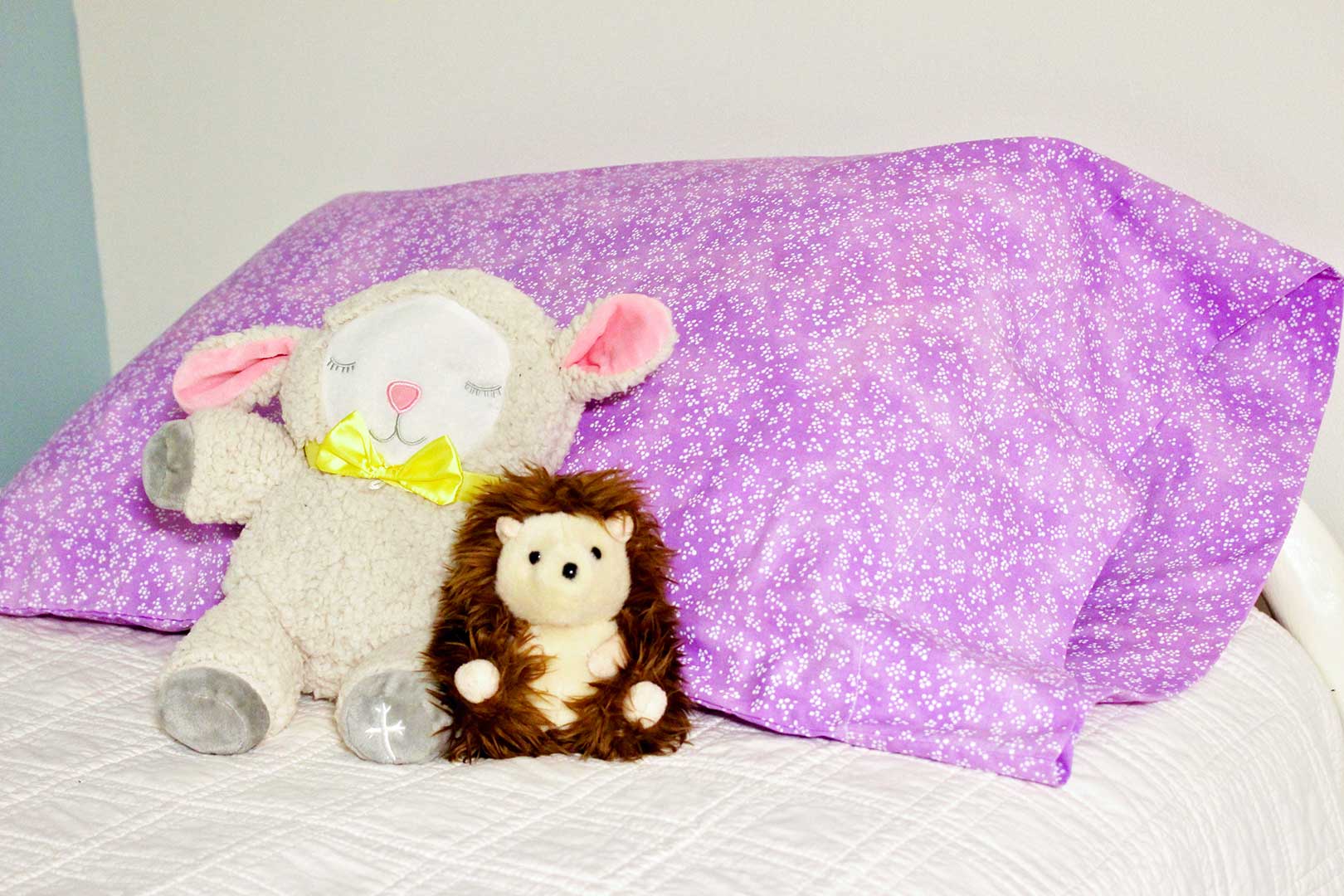 Completed pillowcase on a bed with two stuffed animals resting on it.