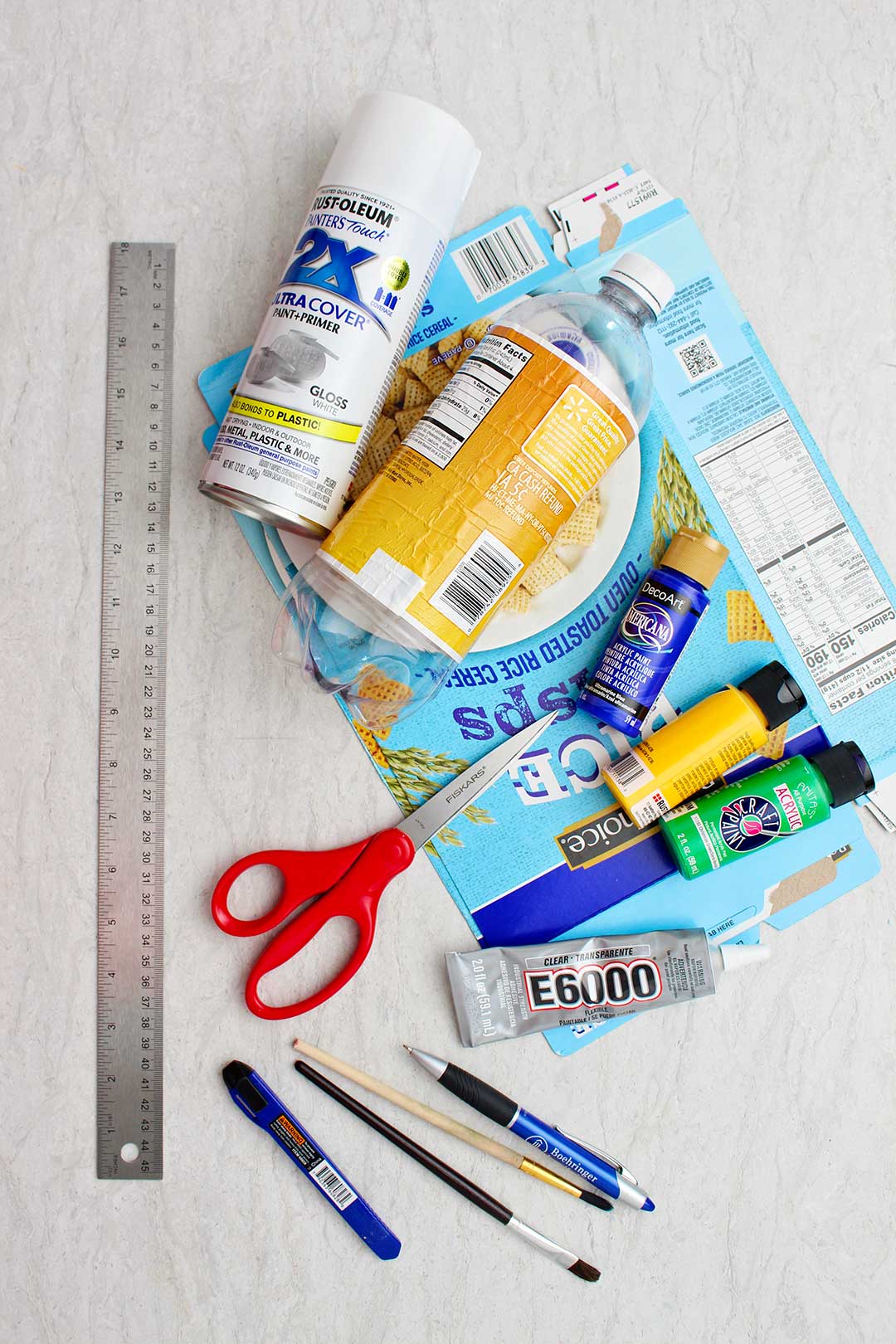 Supplies for a plastic bottle airplane. White spray paint, empty plastic soda bottle, flattened cardboard cereal box, paints, scissors, ruler, and glue.