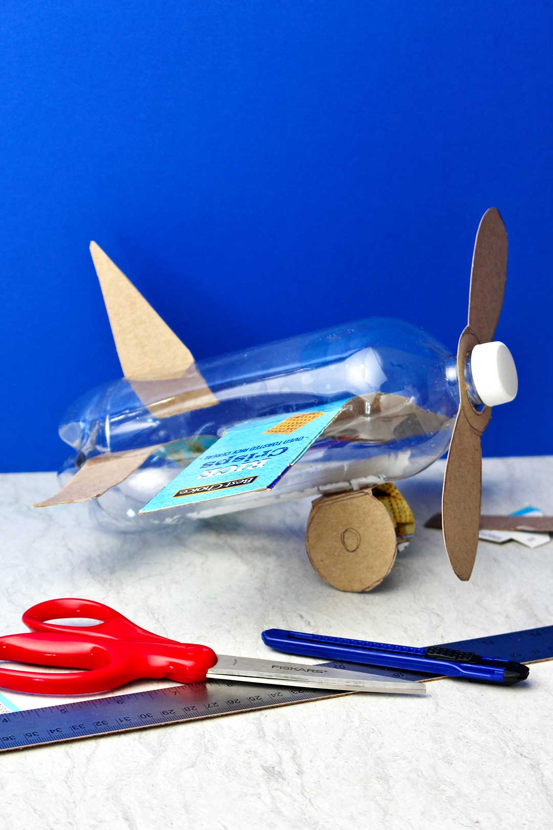Completed bottle airplane before spray painting against a blue backdrop.