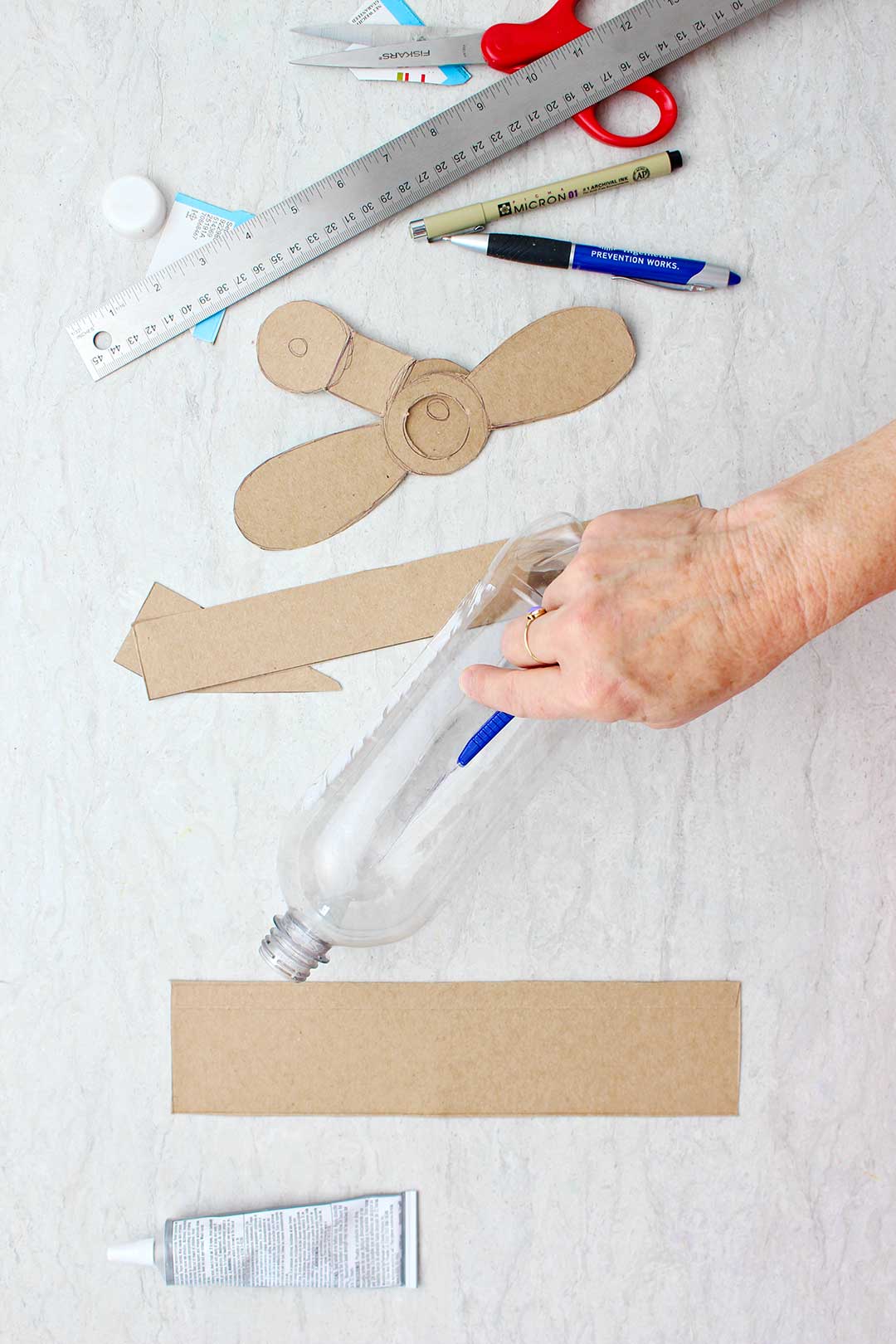 Hand using box cutter to slice a line through the empty plastic bottle with card board wings and propellars near by.