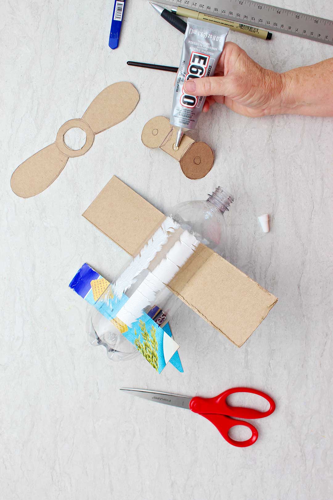Hand gluing pieces of cardboard cut to resemble wheels for the bottom of the bottle.