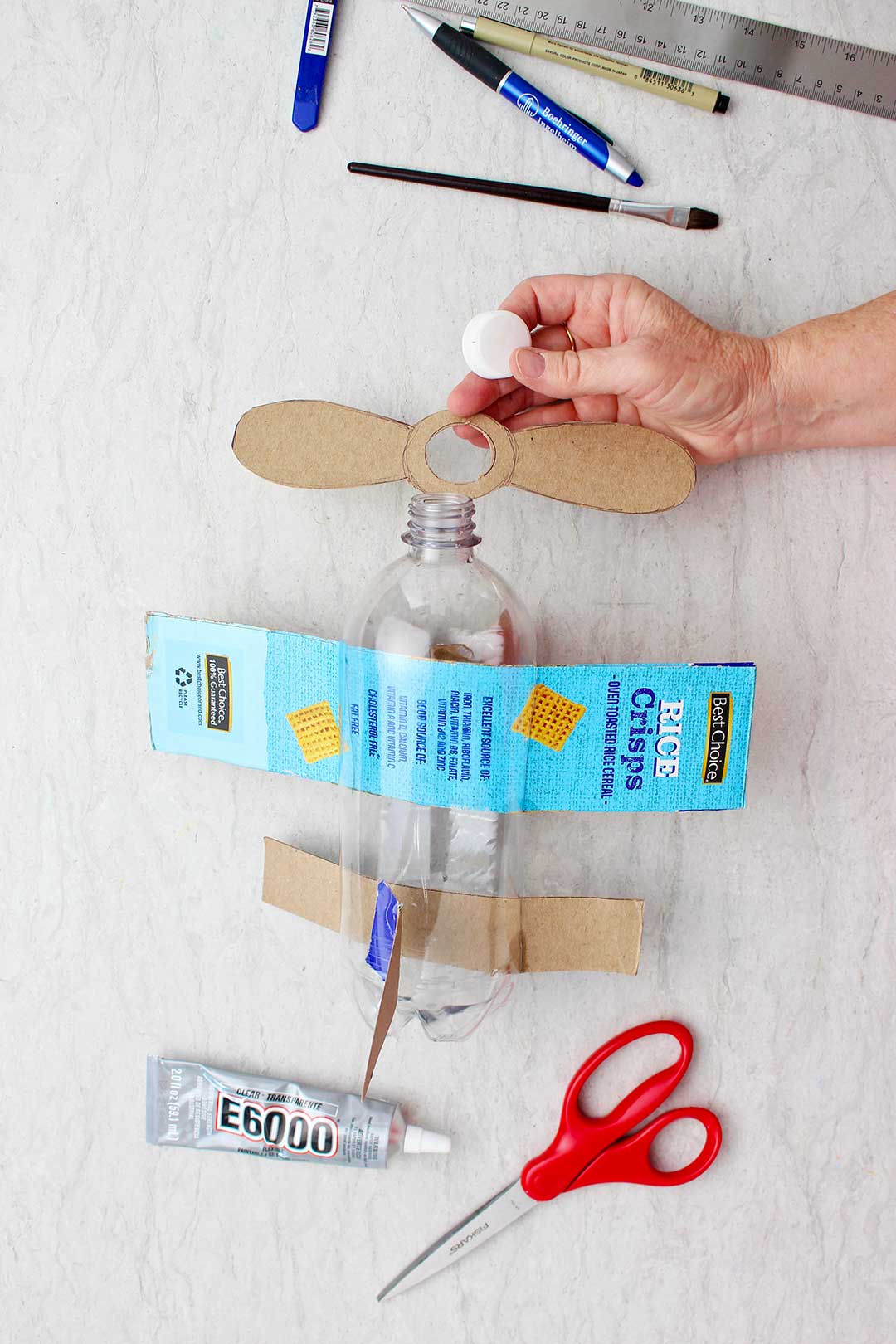 Hand attaching cardboard propellers to the bottle neck.