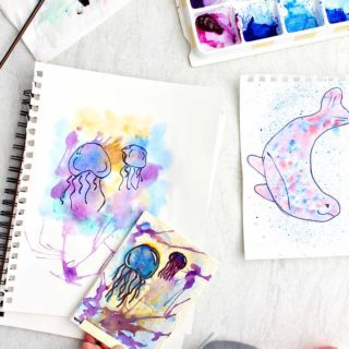 Three completed watercolor paintings using different techniques with supplies near by.