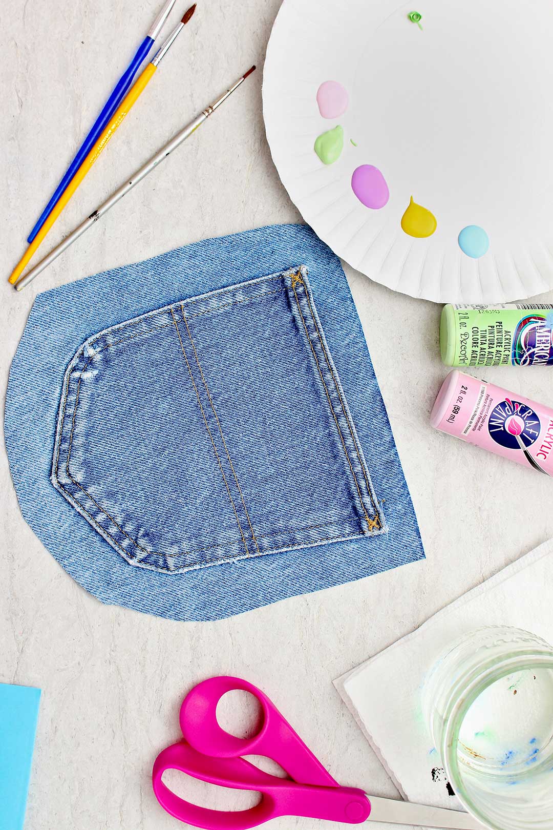 Cut out jeans pocket, a paper plate of acrylic paint swatches and other supplies.