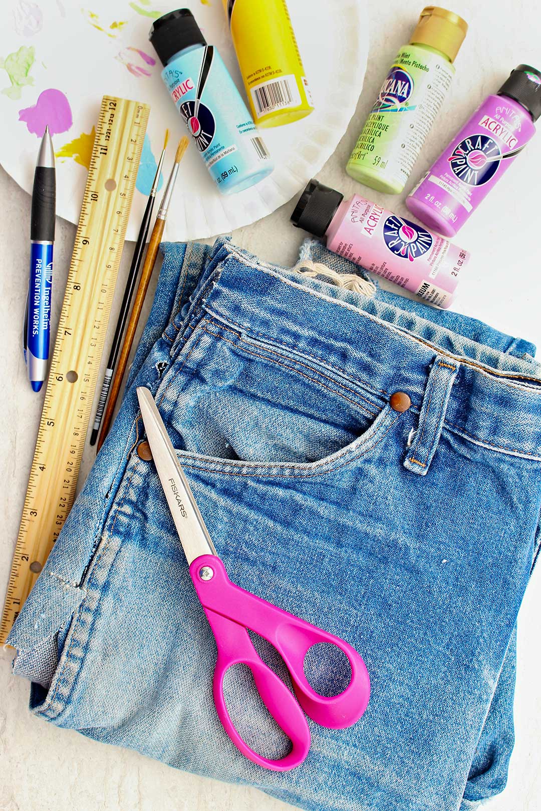 Jeans, pink scissors, acrylic paints, ruler, paintbrushes and pen.