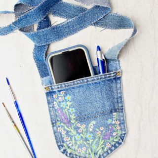 Completed jeans pocket purse with cell phone and pen inside and paintbrushes and ruler near by.