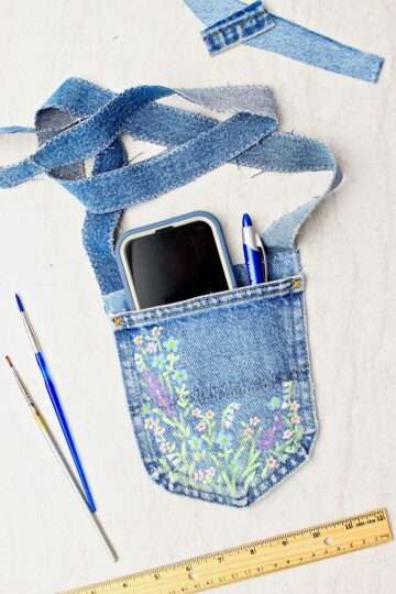 Completed jeans pocket purse with cell phone and pen inside and paintbrushes and ruler near by.