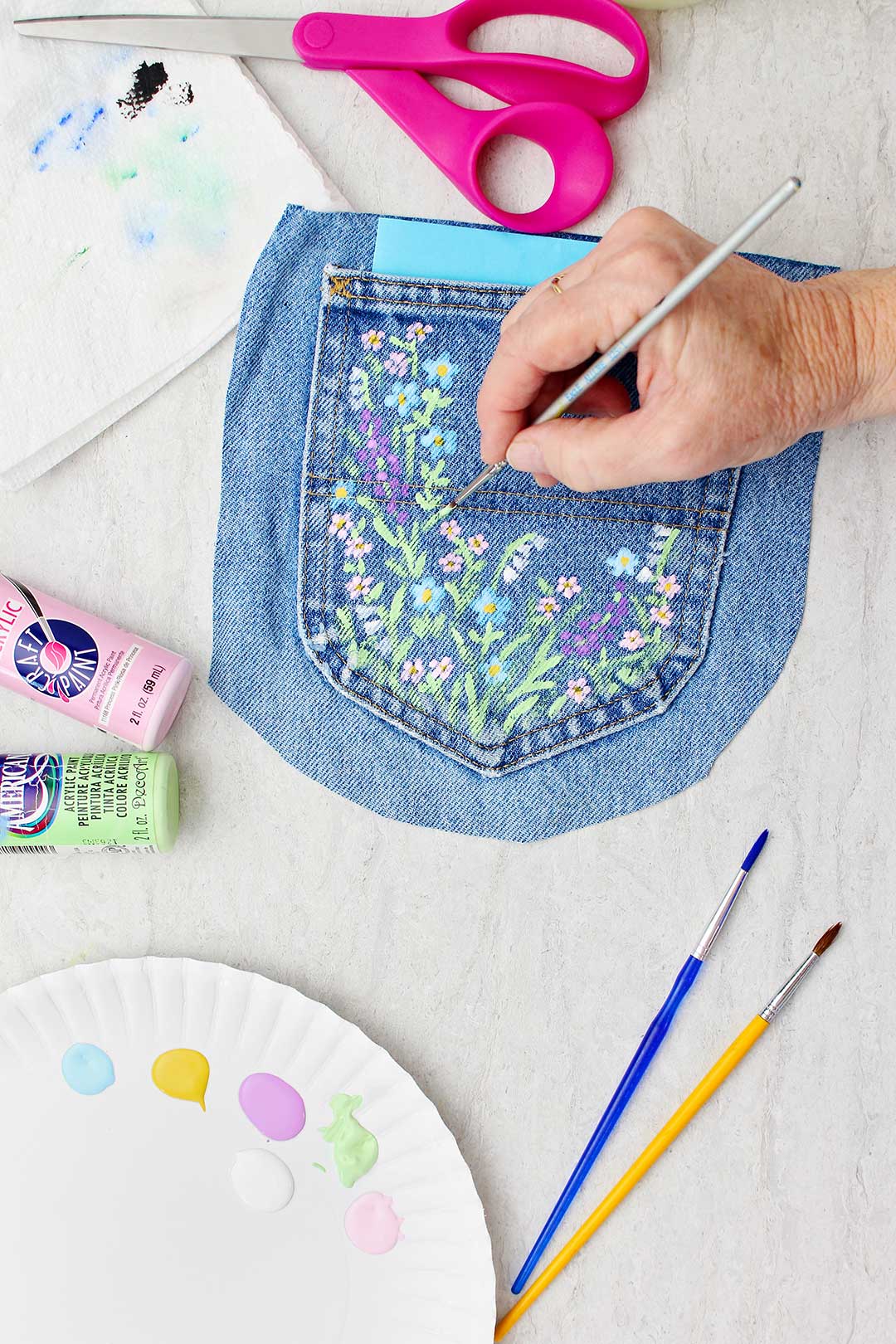 Hand painting small details of flowers on jeans pocket.