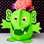 Completed Monster Milk Jug Halloween Decoration standing up against a black and pink polka dotted background.