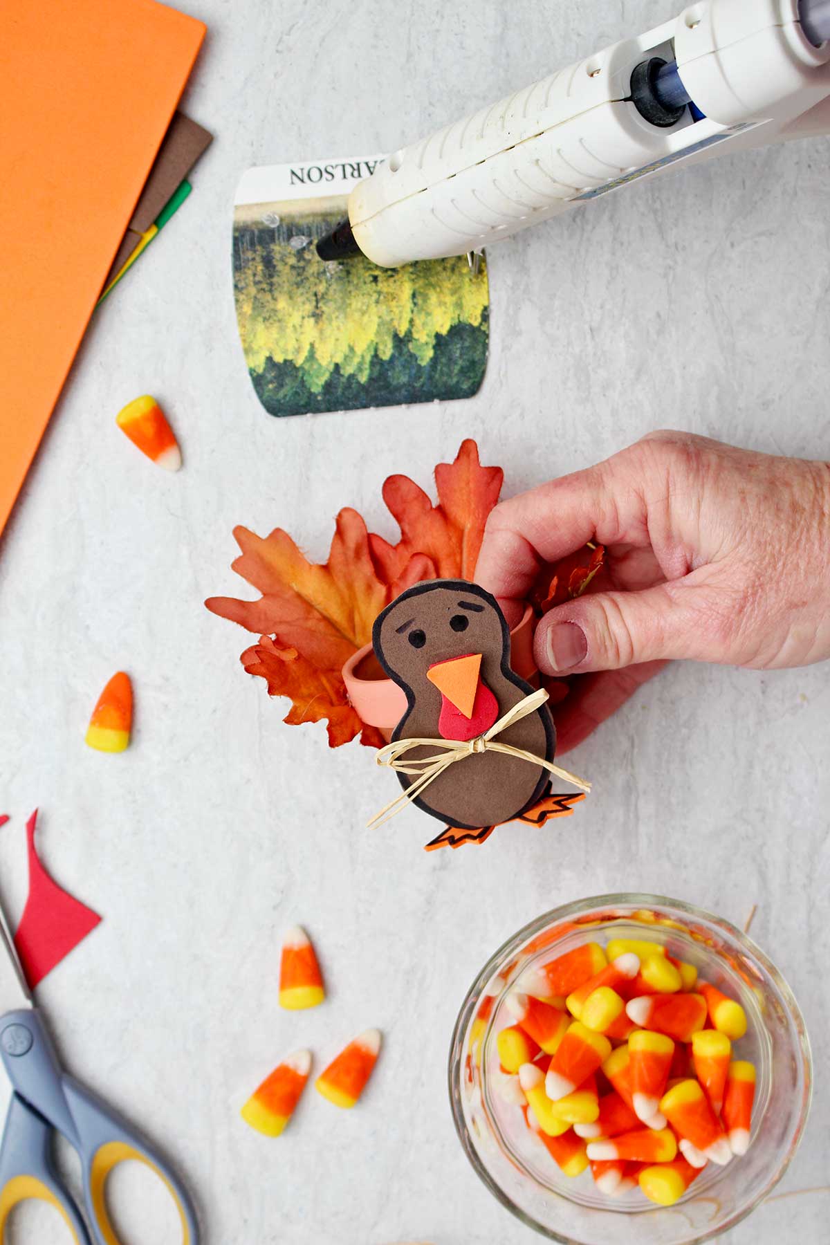 Hand holding a completed Flowerpot Turkey Thanksgiving Favor with supplies near by.