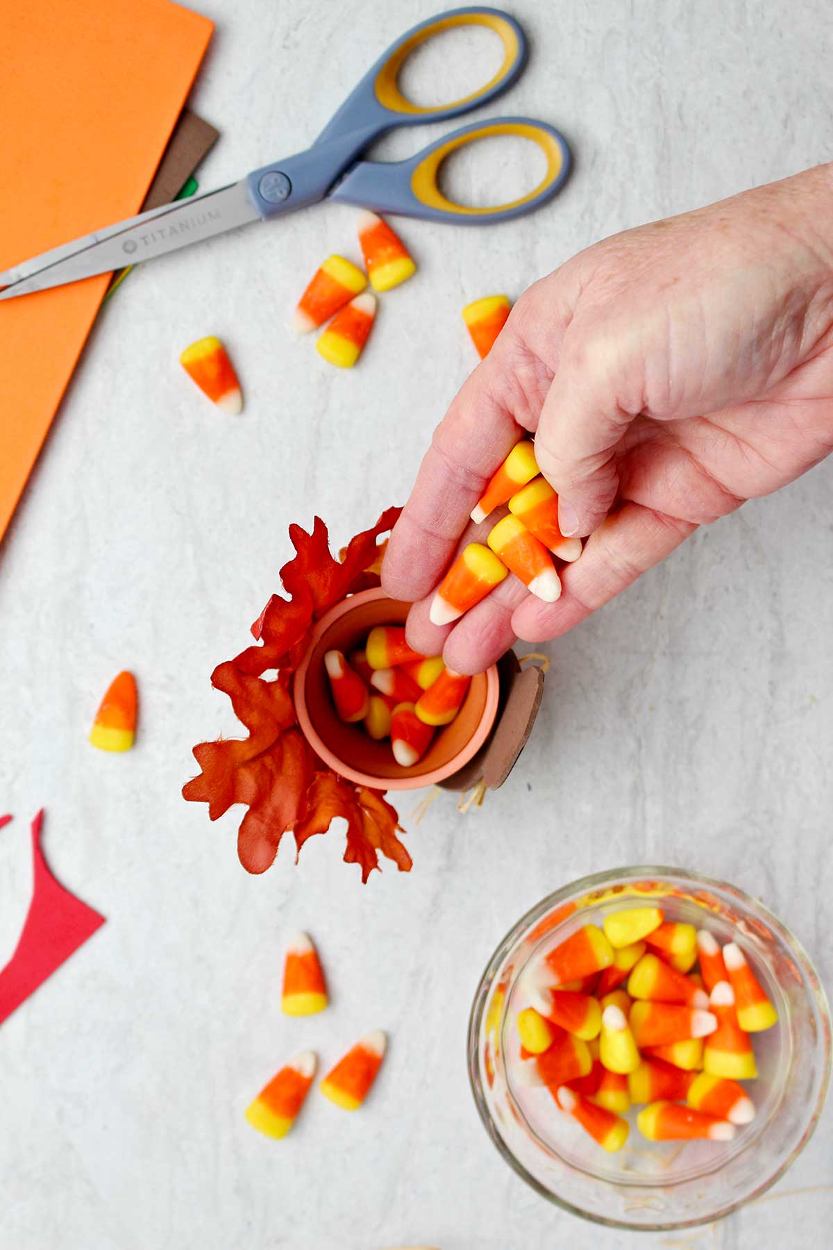 Hand placing candy corn in the flowerpot of the completed Thanksgiving favor with other supplies near by.