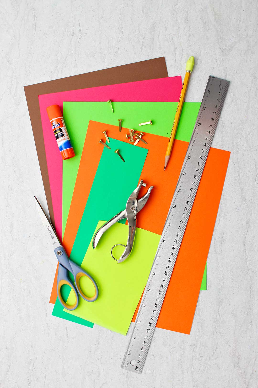 Different colored papers, metal ruler, pencil, scissors, hole punch, metal brads and glue stick.