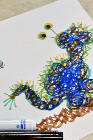 A blue scribble monster on a piece of paper with markers.