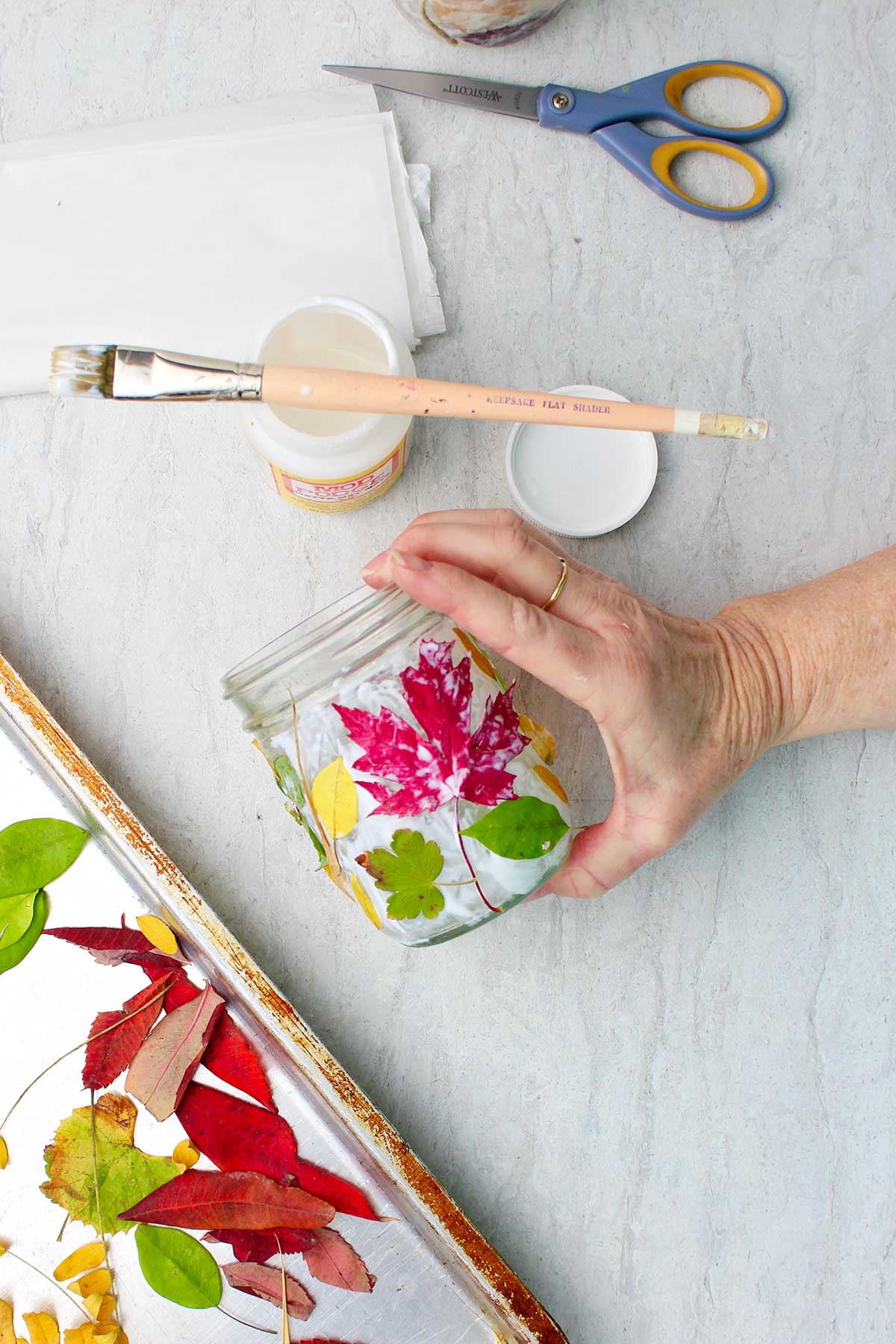 Hand holding mason jar with leaves as Mod Podge dries.