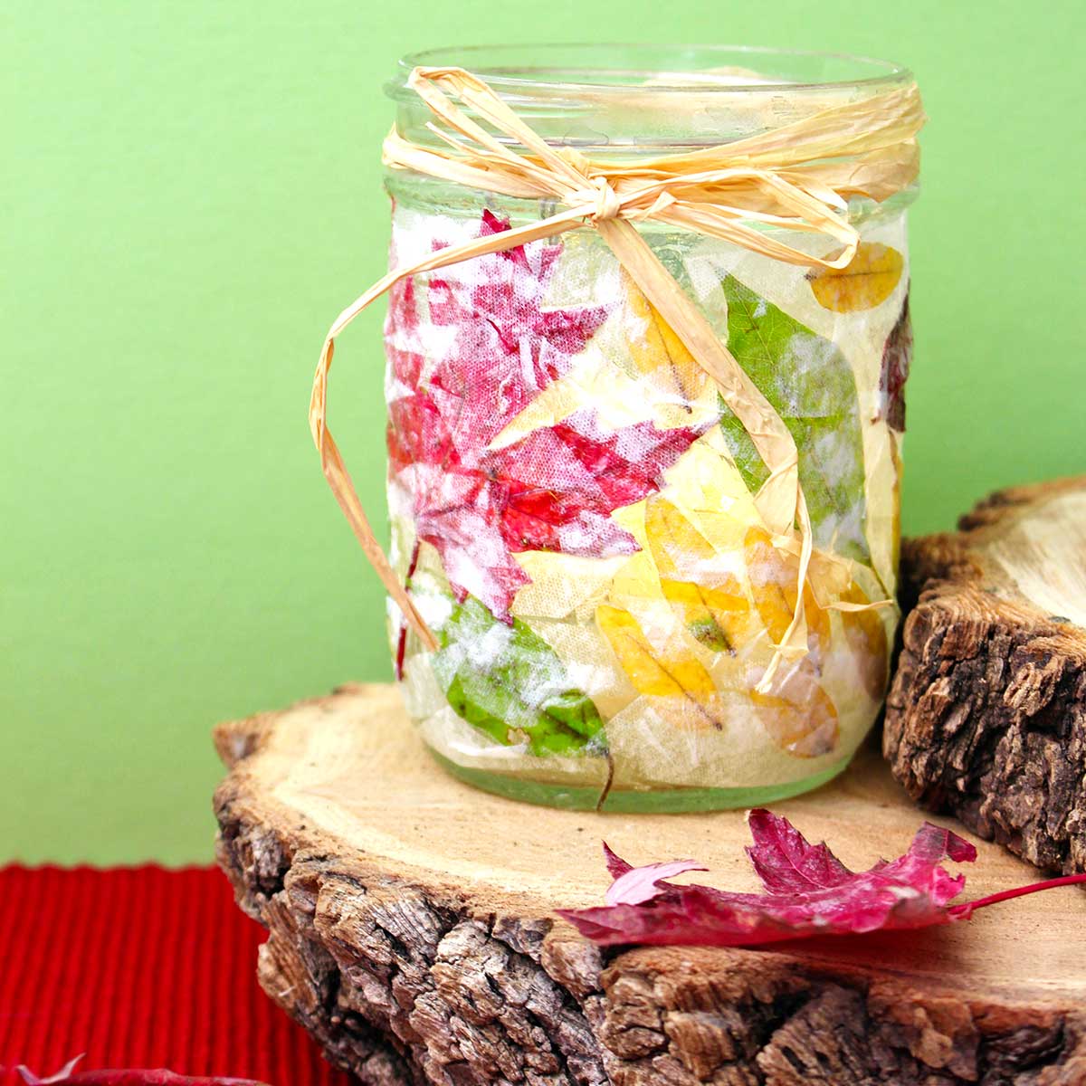 Completed Fall Leaf Mason Jar Candle Holder sitting on a stump in front of a lime green background. Square image.