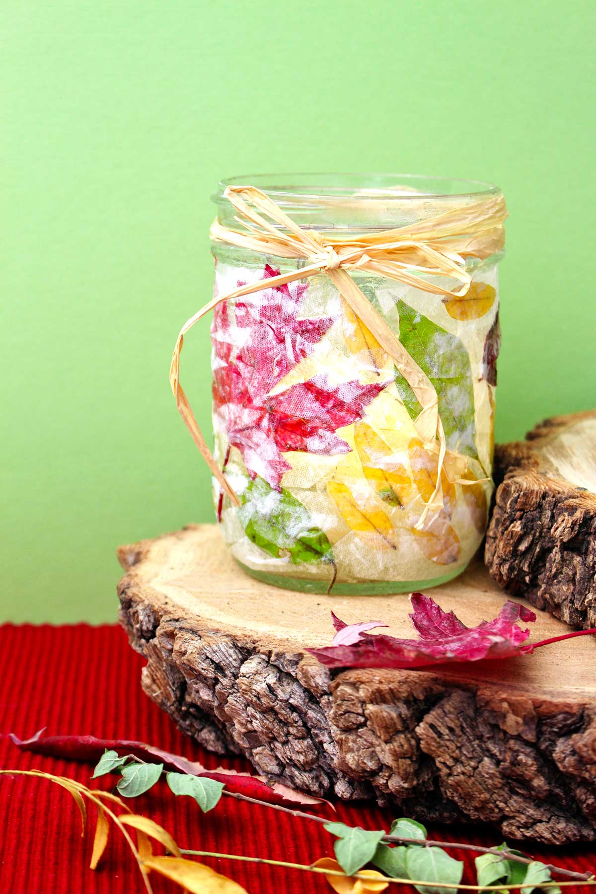 Completed Fall Leaf Mason Jar Candle Holder sitting on a stump in front of a lime green background.