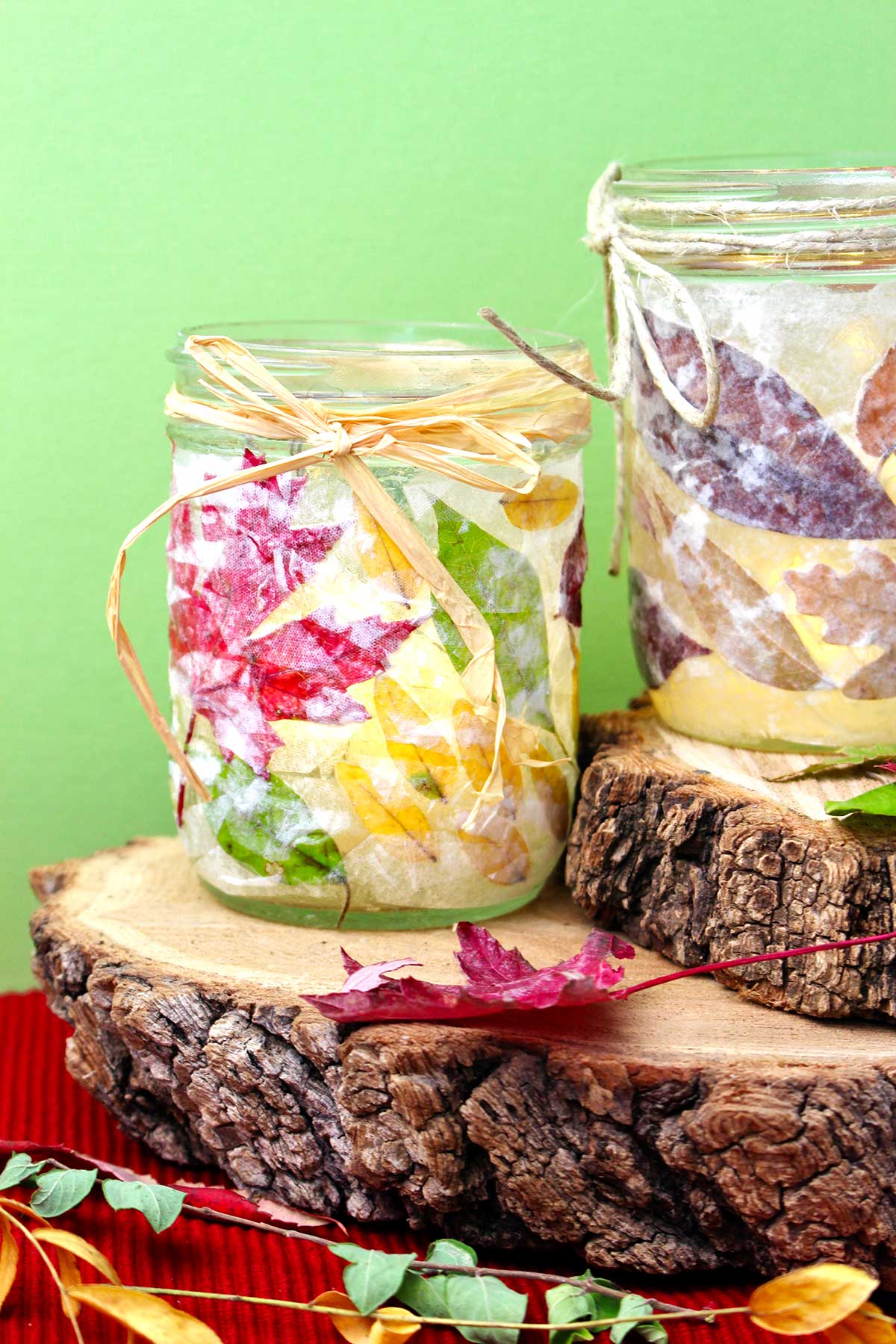 Two completed Fall Leaf Mason Jar Candle Holders on stumps of wood against a lime green background.