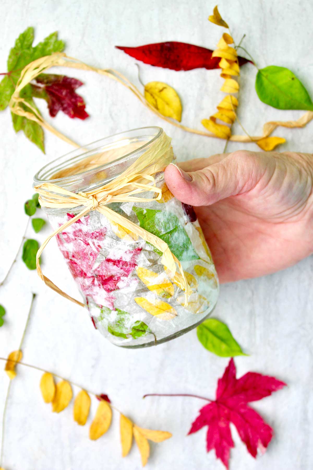 Hand holding completed Fall Leaf Mason Jar Candle Holder tied with twine.