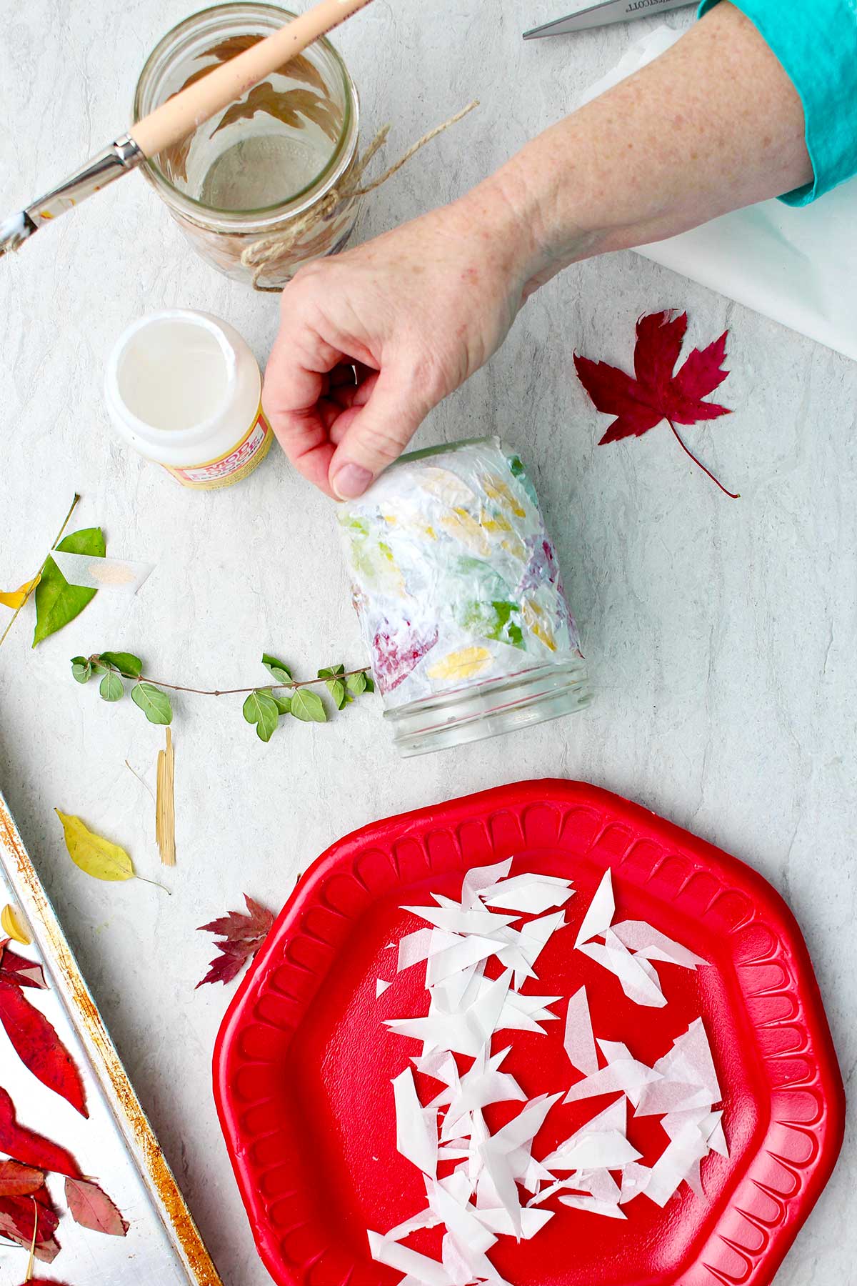 Hand placing paper towel on Mod Podge painted leaves on a mason jar.