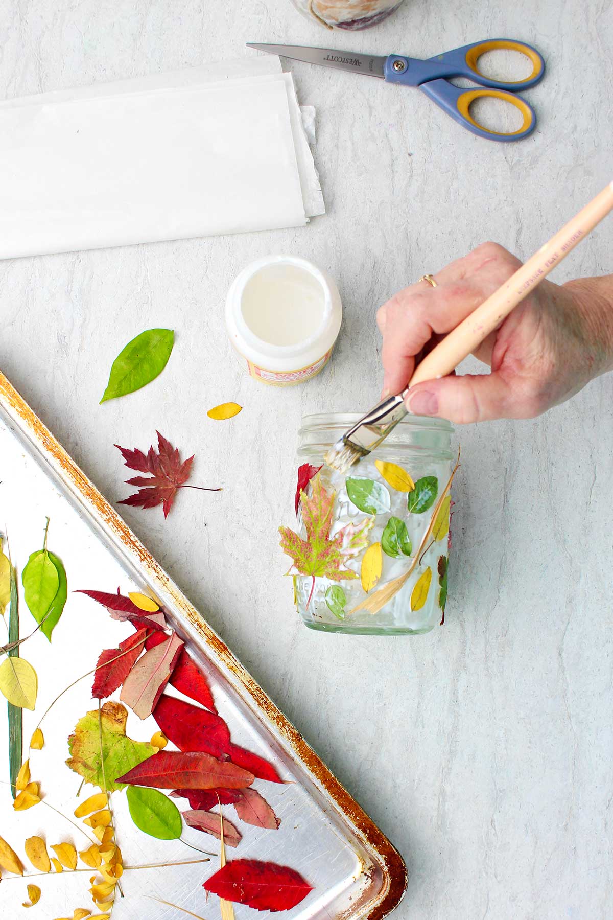 Hand painting Mod Podge on mason jar covered in leaves.