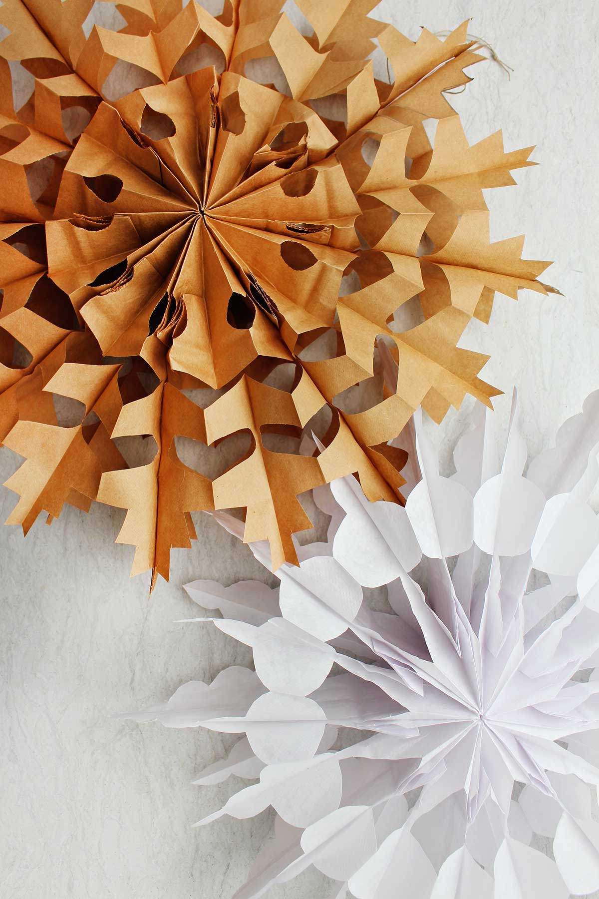 Two completed paper bag snowflake. One in brown and one in white.