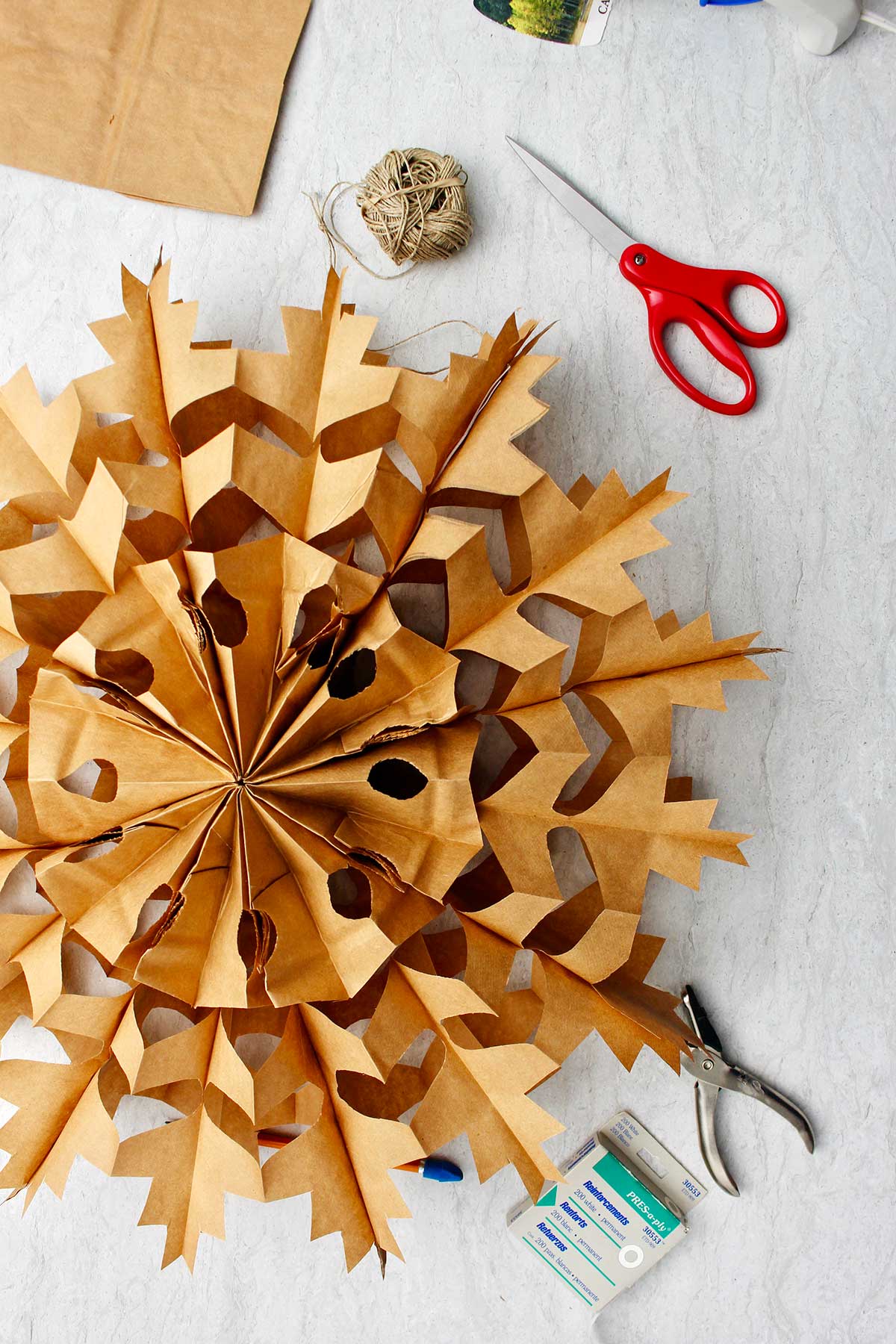 Completed brown paper bag snowflake with supplies near by.