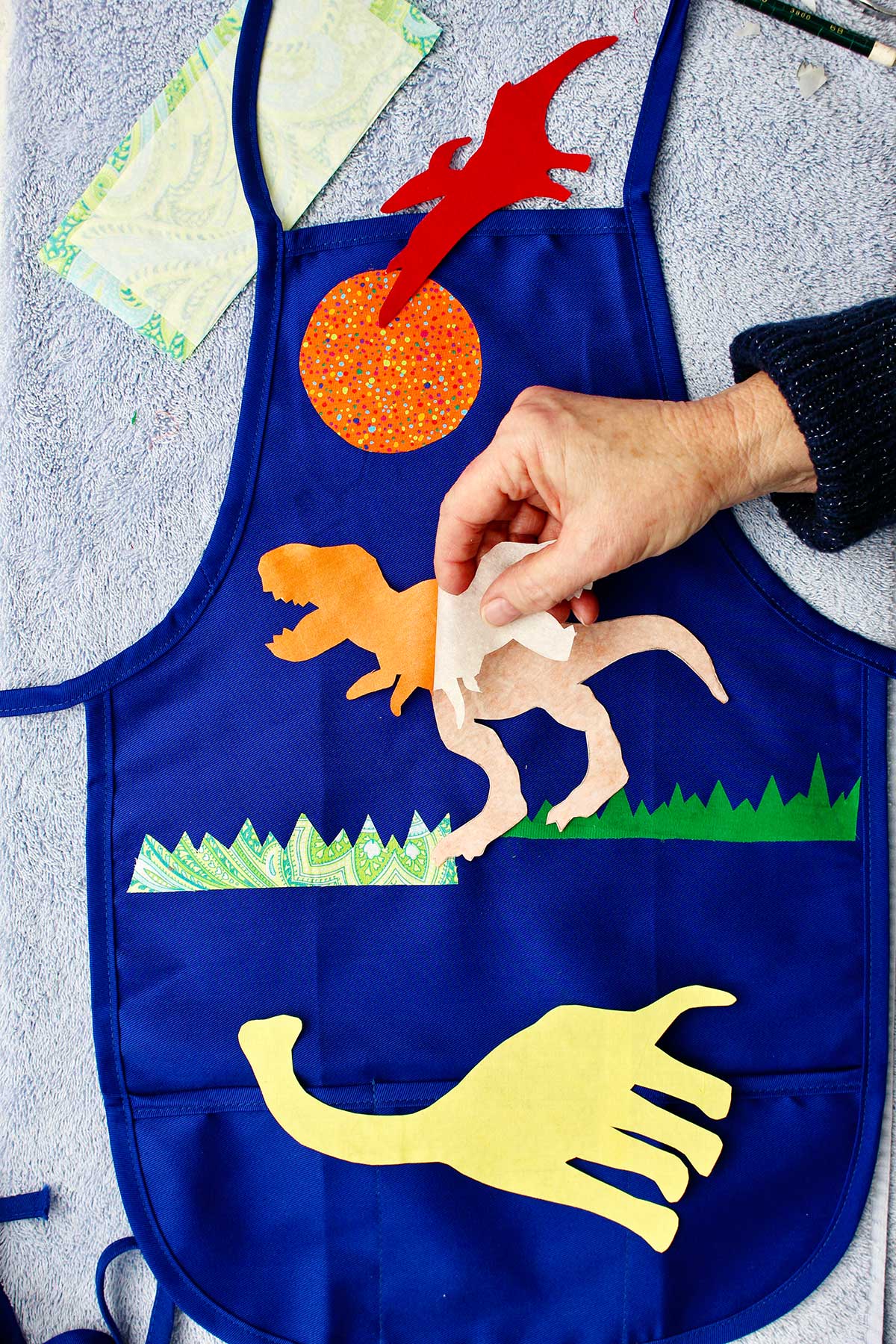 Hand peeling back appliqué paper from t-rex fabric.