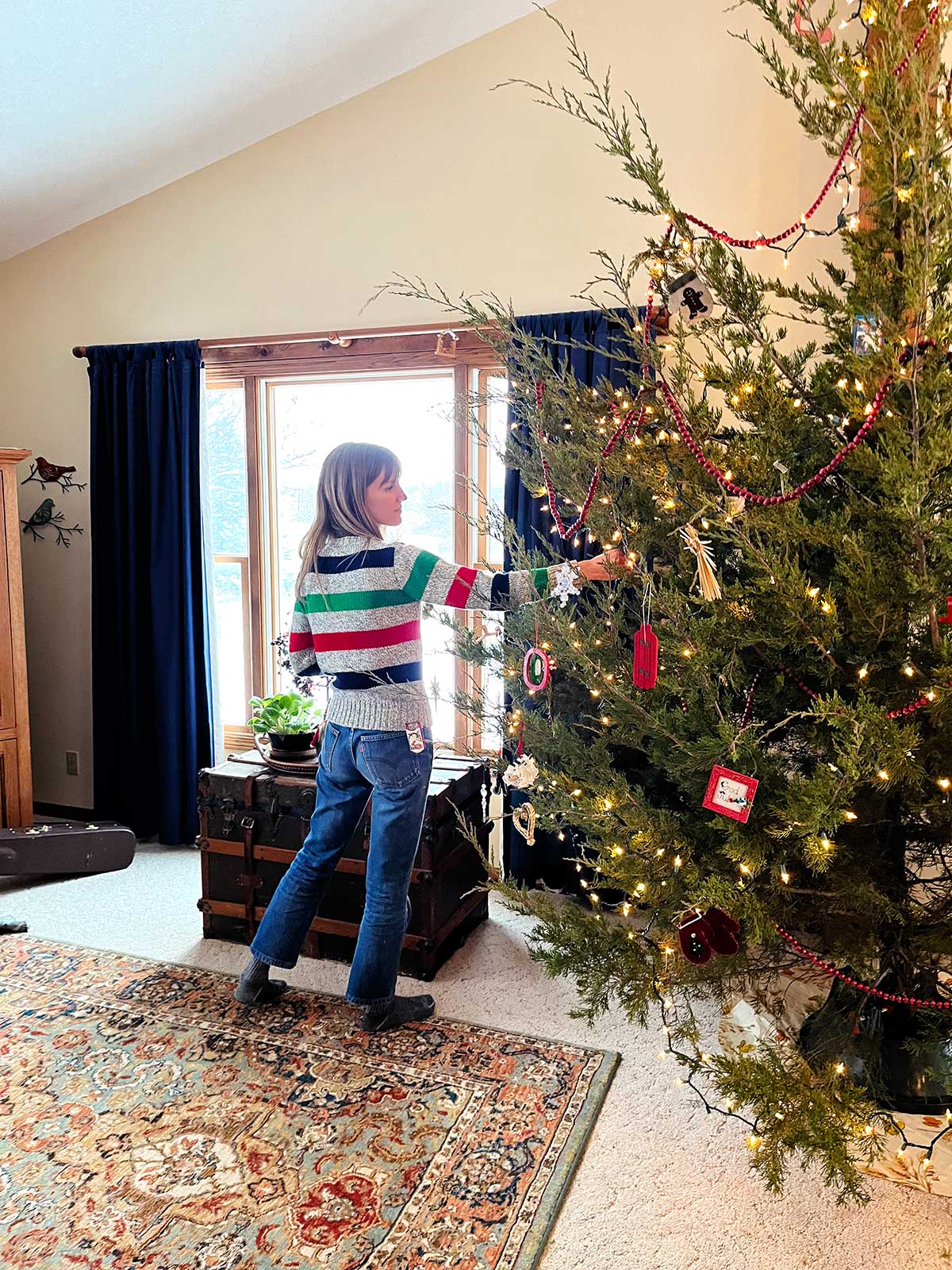 Woman in striped sweater hangs ornament on Christmas tree.