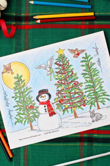 Completed Christmas tree coloring page resting on a green and red placemat with white decorative bells near by. Square image.