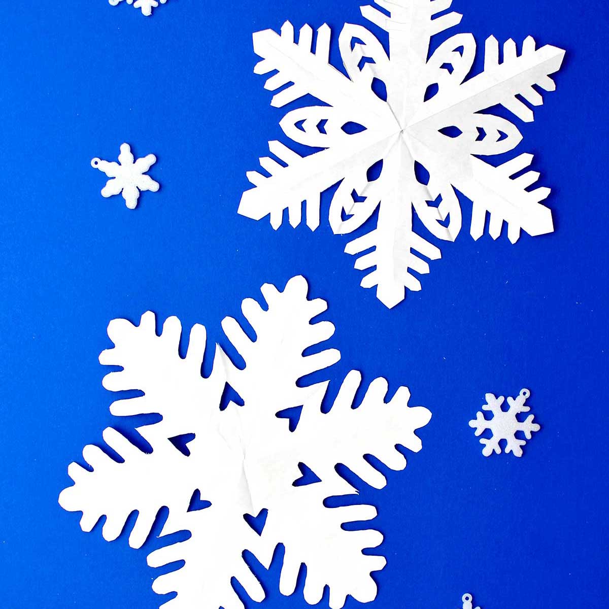 Two completed snowflakes made from white paper resting on blue background.