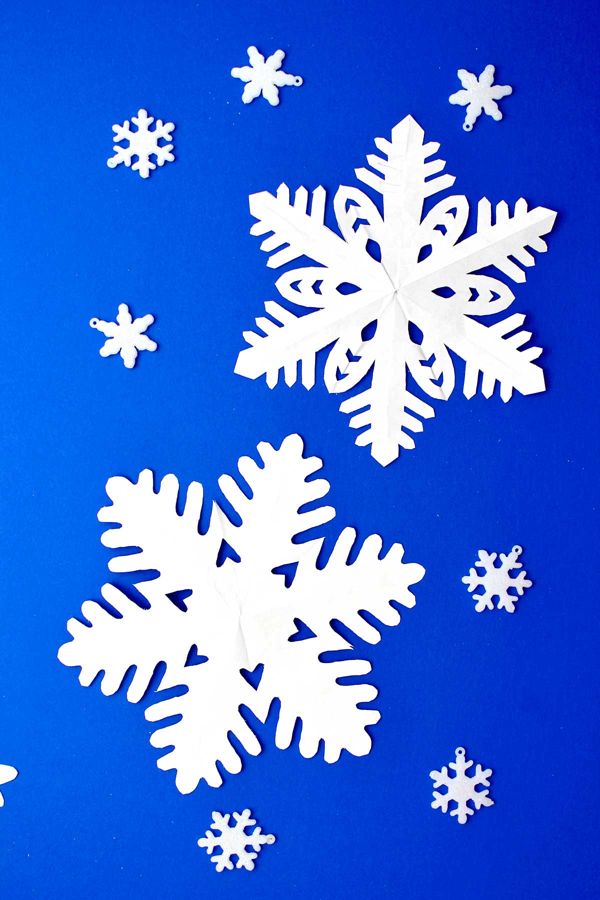 Two completed snowflakes made from white paper resting on blue background.