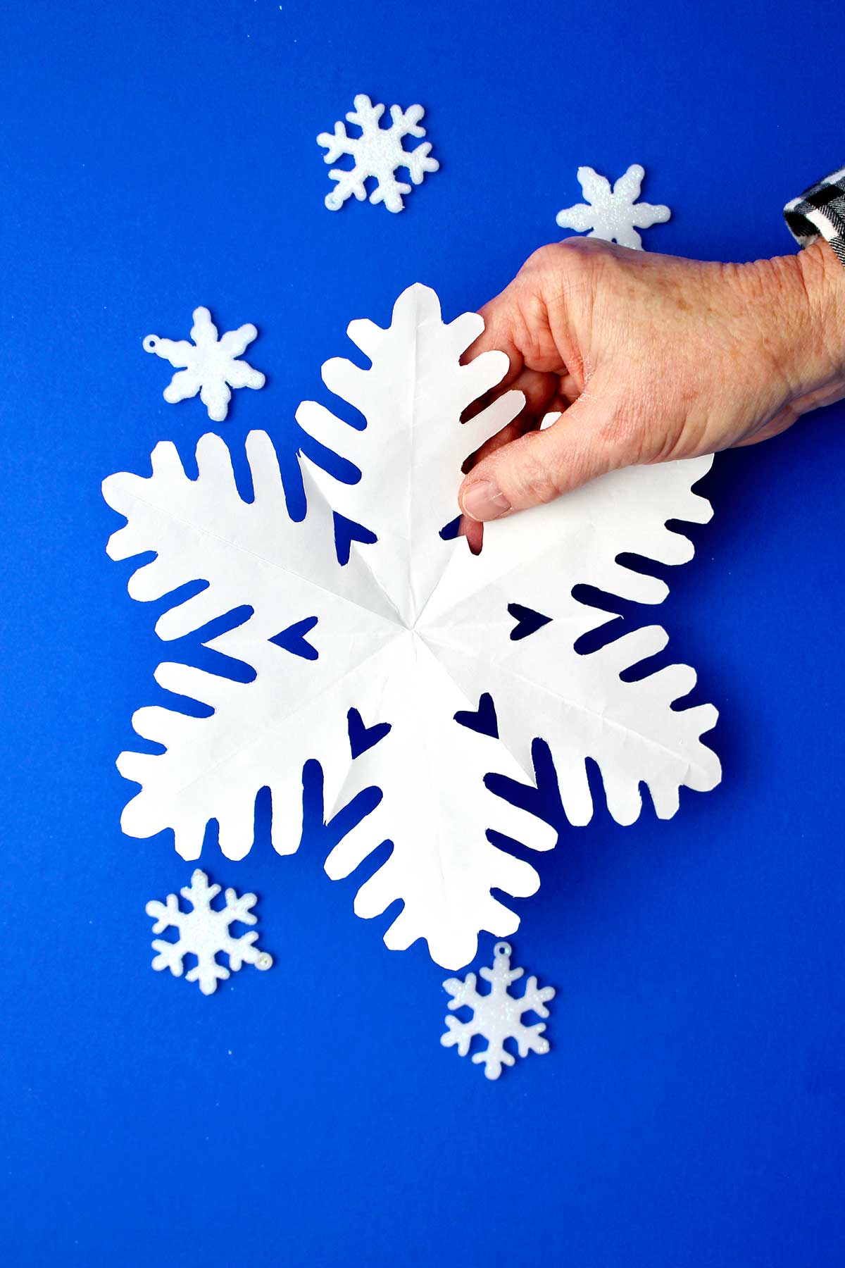 Hand holding fully unfolded snowflake made from white paper.